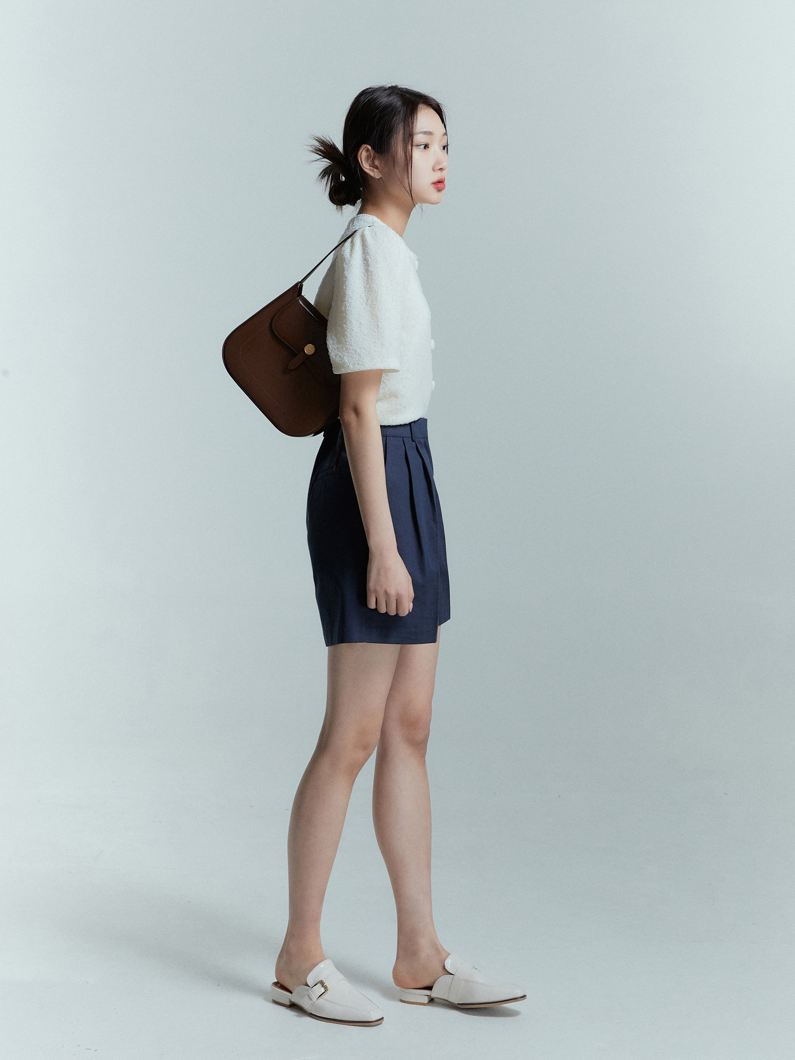 A side capture of a model wearing the navy pleated trouser shorts showing the side look of the product.