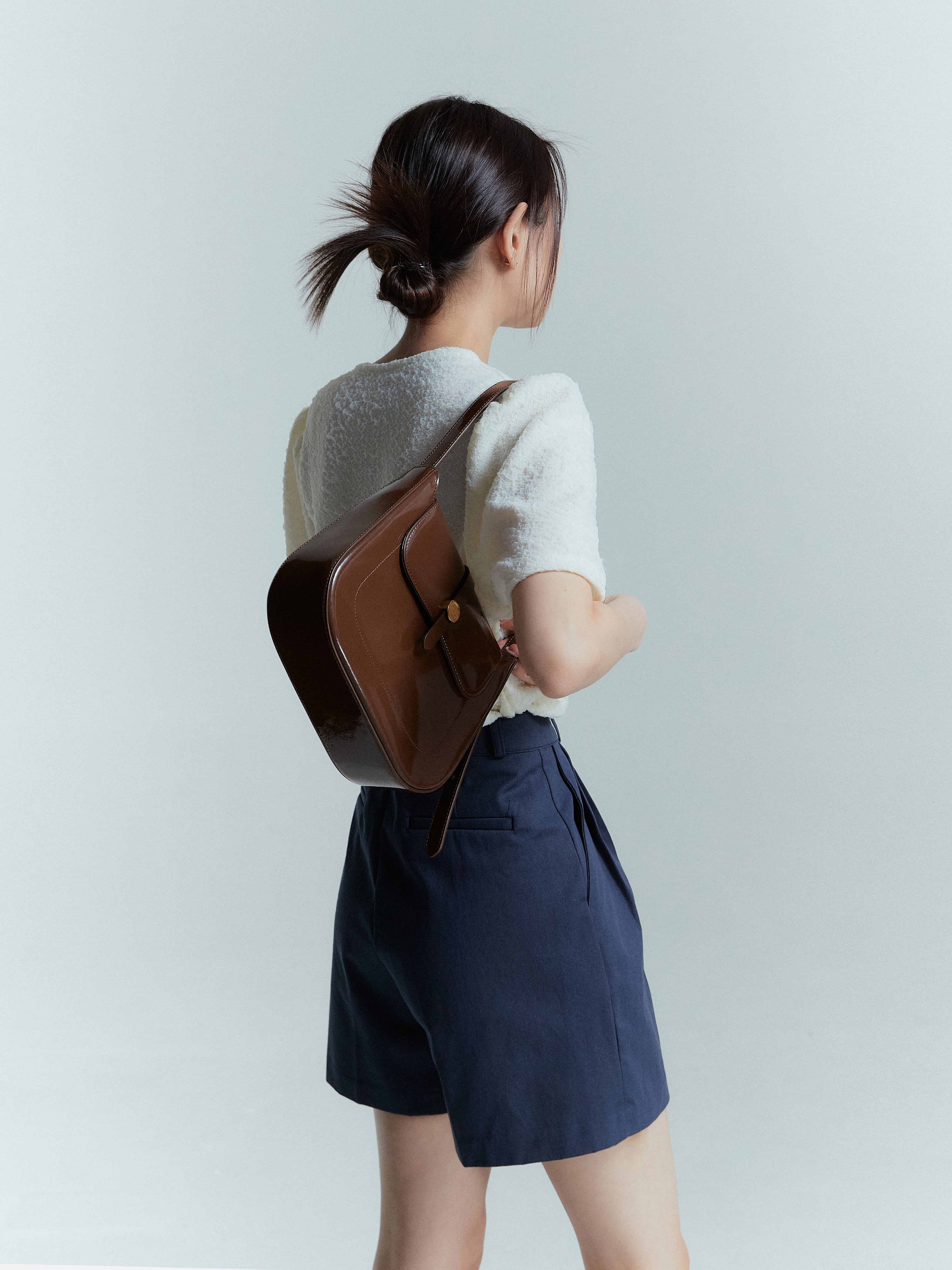 A slight side-angled shot of a model showcasing the navy pleated trouser shorts styling it with leather bag.