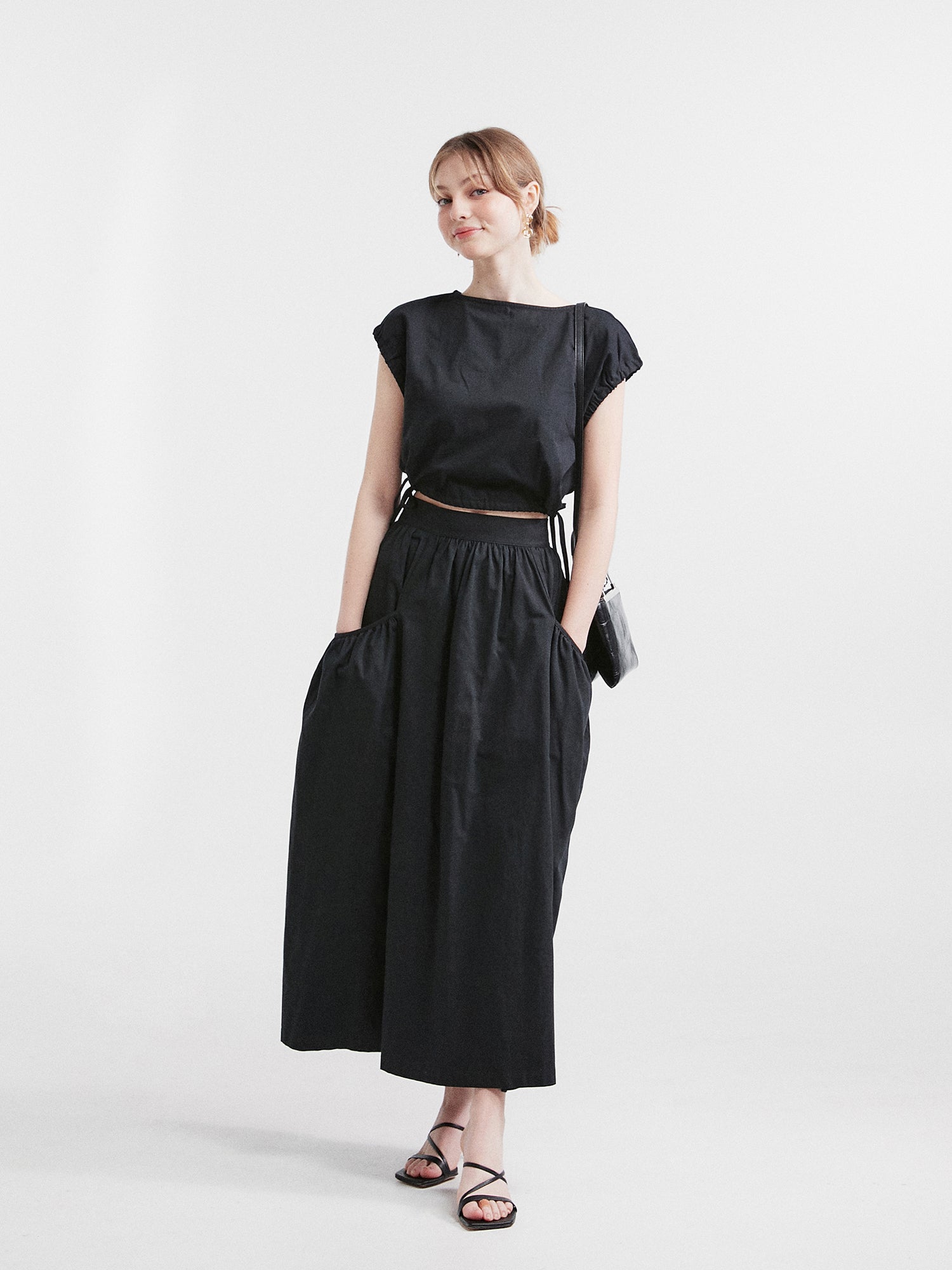 Full shot of a model in a Korean aesthetic outfit, confidently wearing the black elastic waist crop top, perfectly matching it with the ruched pocket elastic waist skirt.