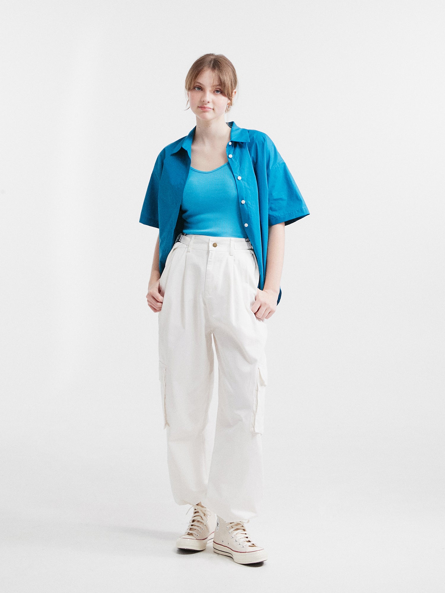 A full-shot of a model wearing the blue button front shirt pairing it with the white cargo pants.