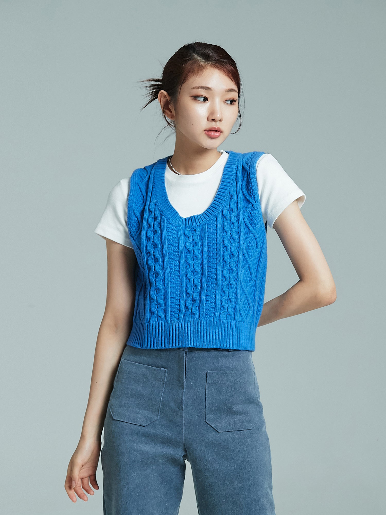 Model looking to the side while wearing the blue cable knit vest.