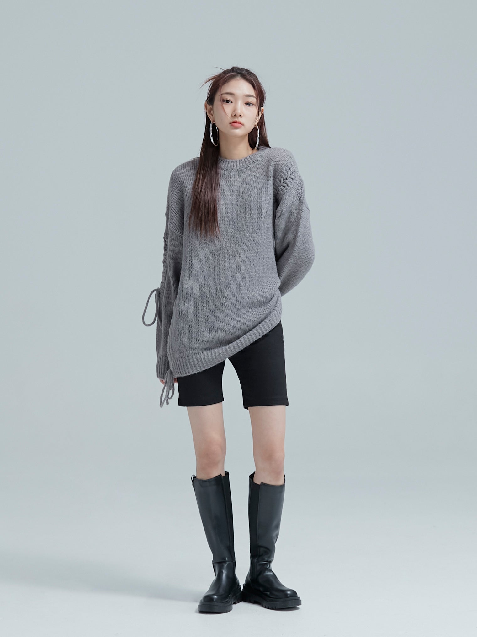 A comprehensive shot capturing the model posing with one side of the cable tie sweater lifted, showcasing a distinctive Korean street fashion vibe.