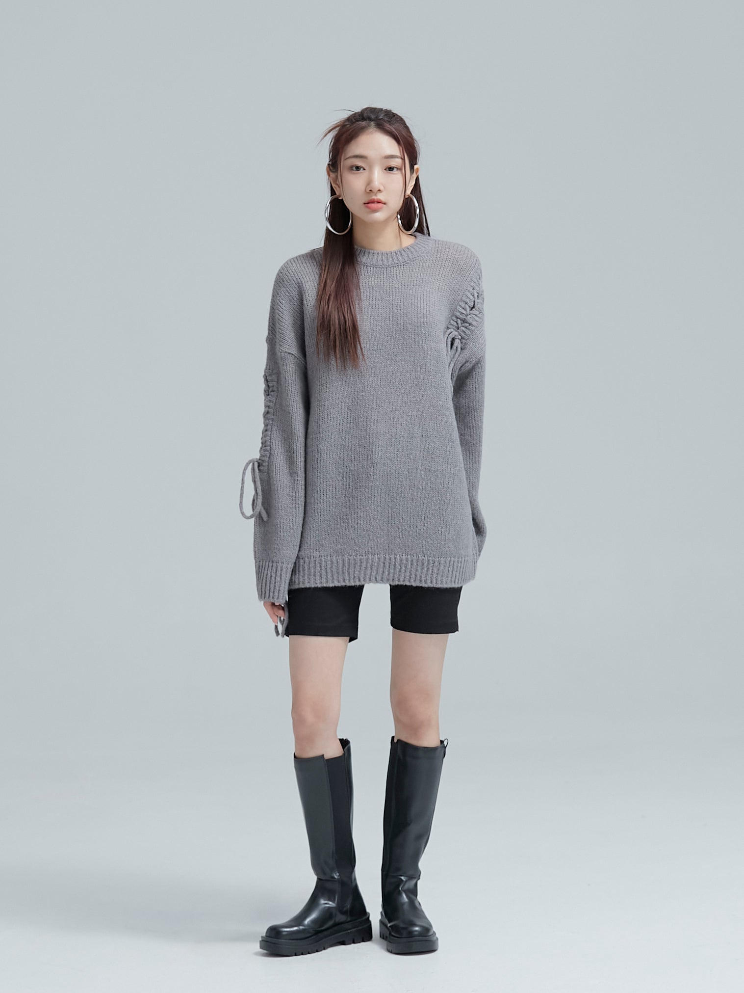 The model is standing still while wearing the cable tie sweater to showcase its korean street style.