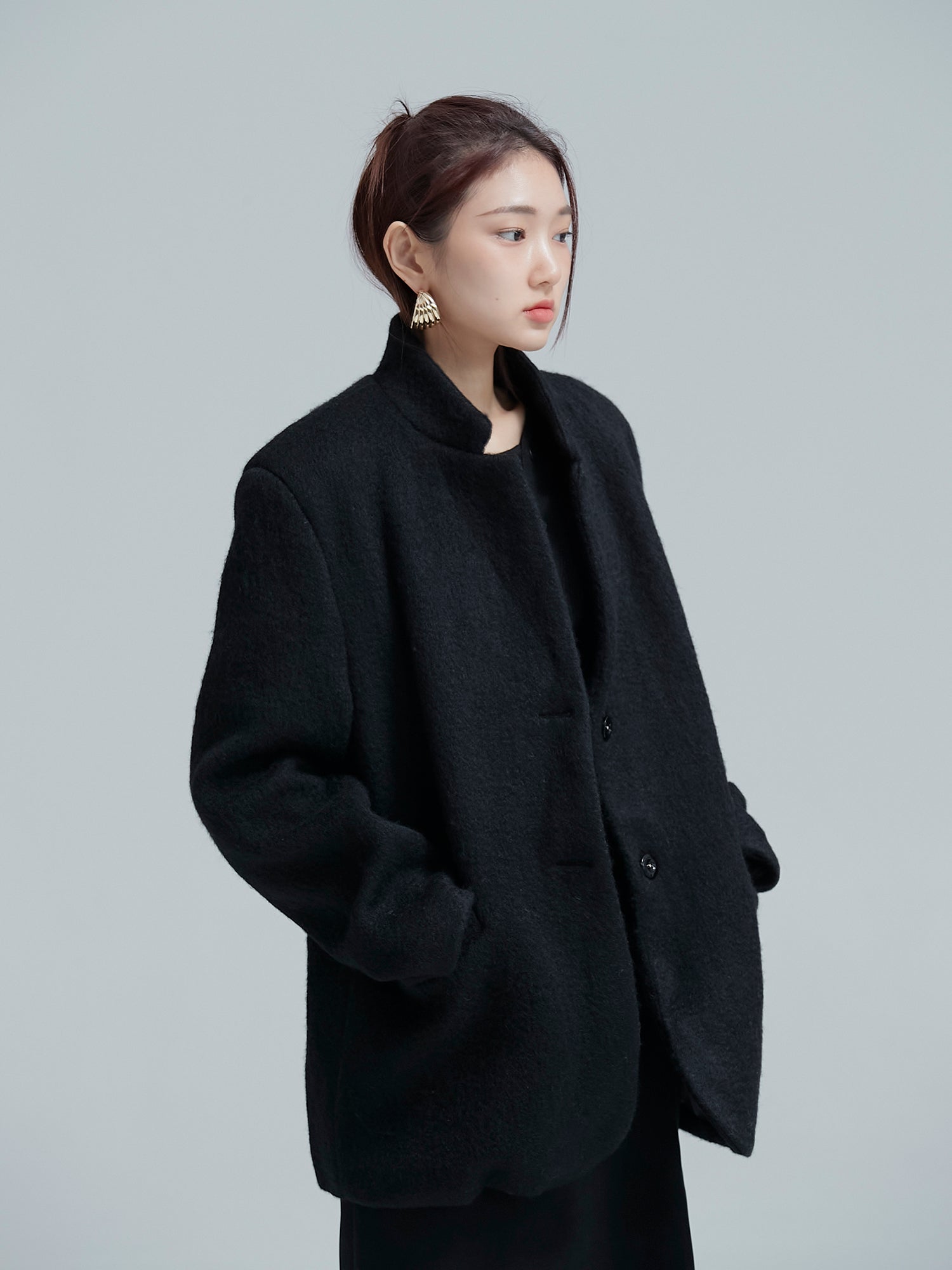 A tilted view of the model wearing the black cocoon jacket while matched with gold striped metal hoop earrings to showcase its korean street fashion.