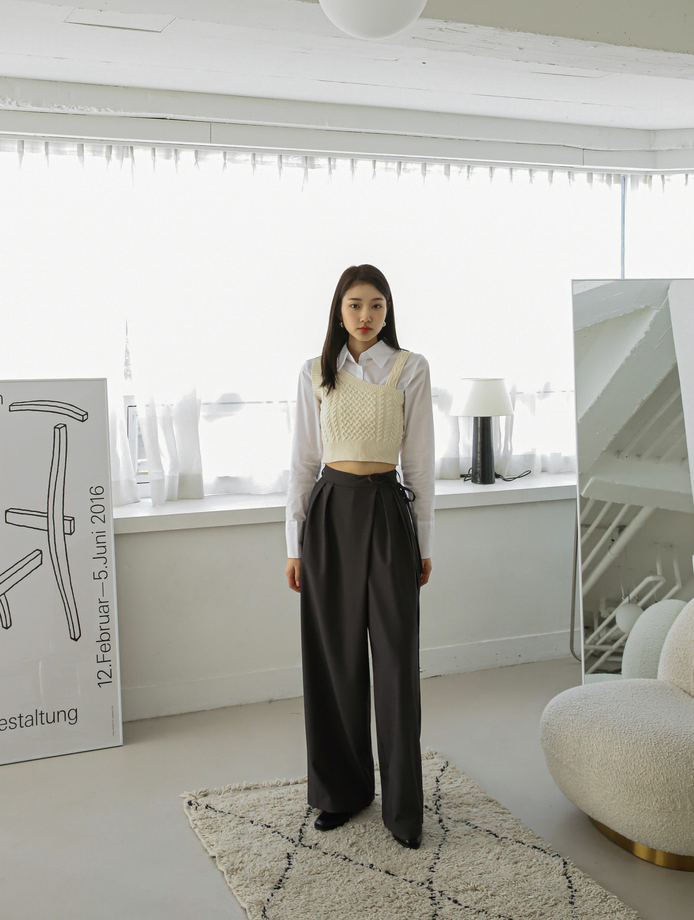 A model standing up wearing a knit tank top with belt tied trouser.