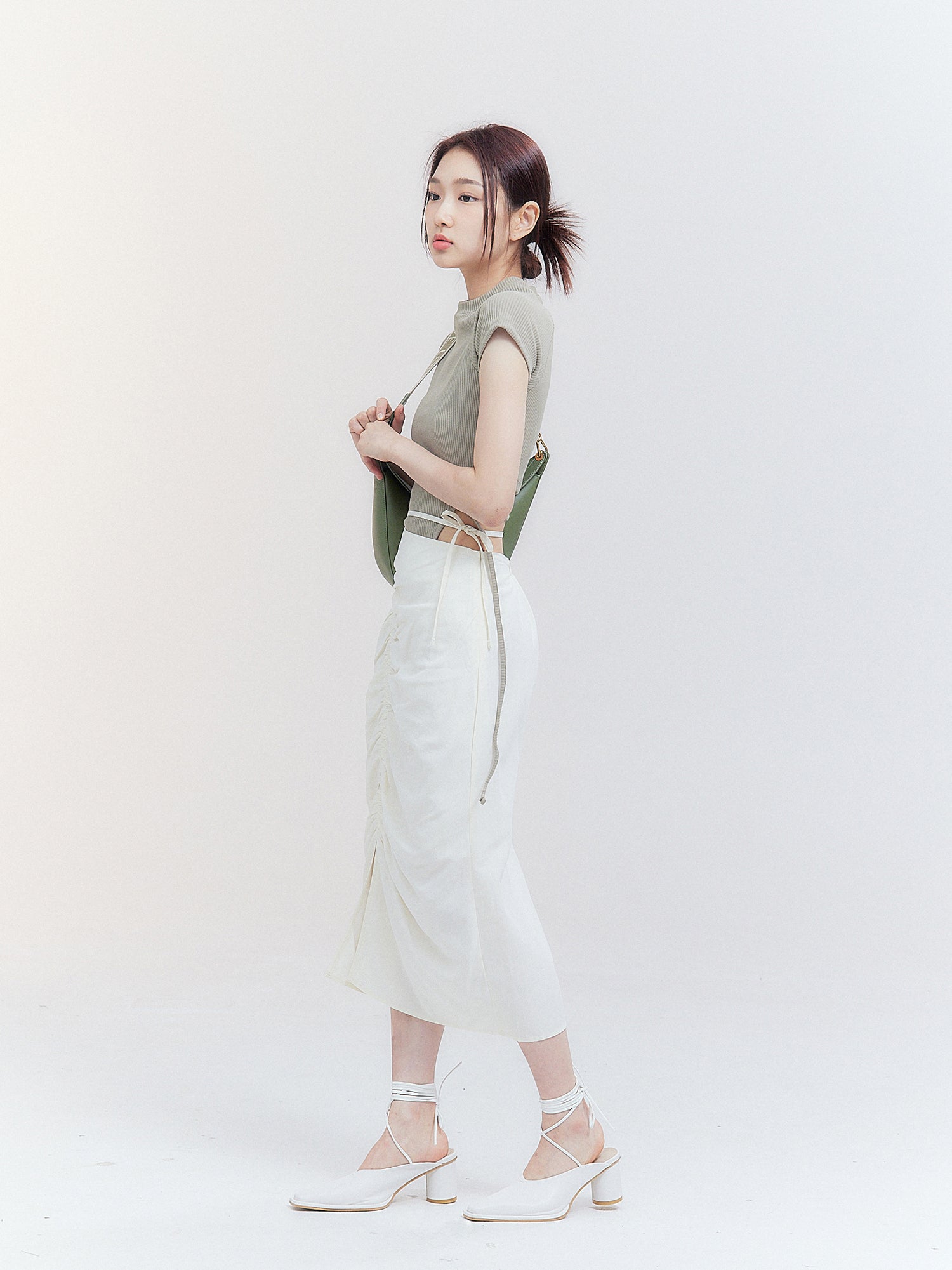 A side view of the model wearing the Crop Top with Strap, elegantly matched with a drawstring skirt, showcasing the side fitting of the top and embodying the essence of Korean street fashion.