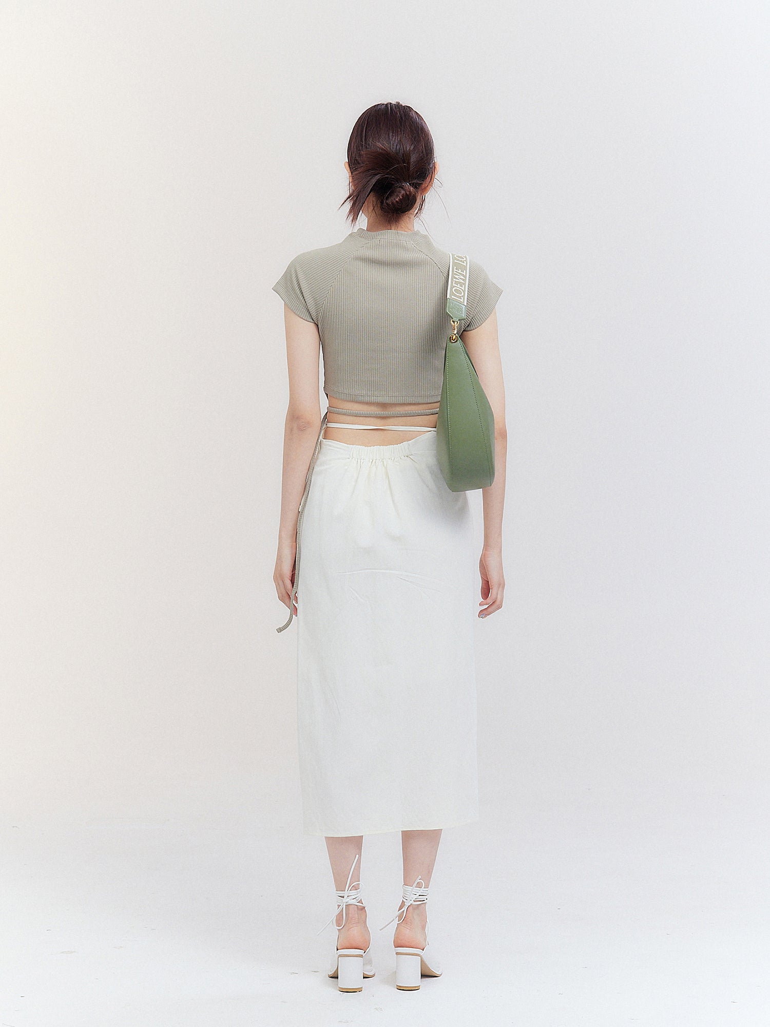 Captured from the rear, the model dons the crop top with strap, exhibiting the detailed design elements on the back of the garment.