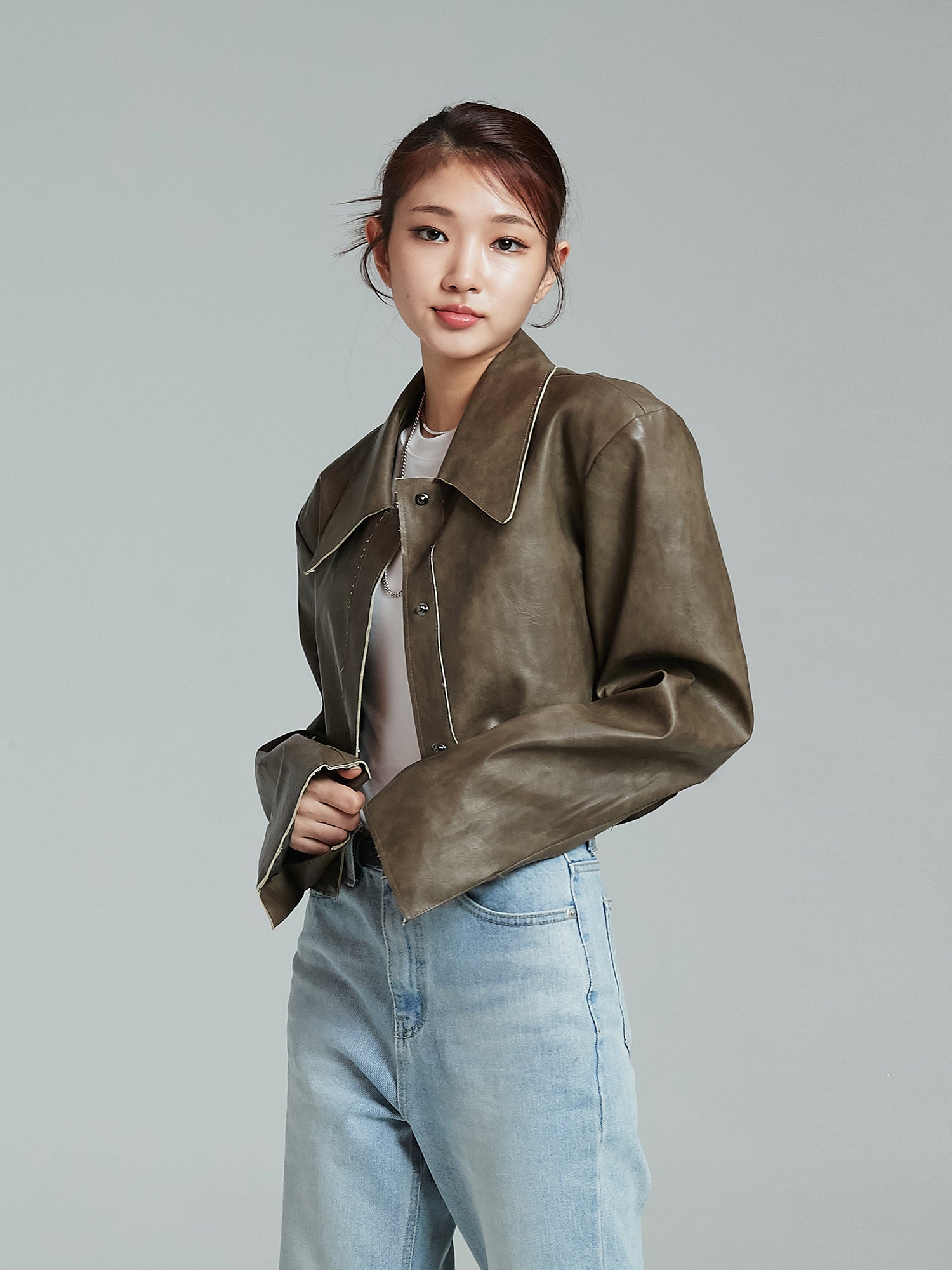 A tilted angle of the model wearing the brown cropped leather jacket showcasing its korean street fashion.