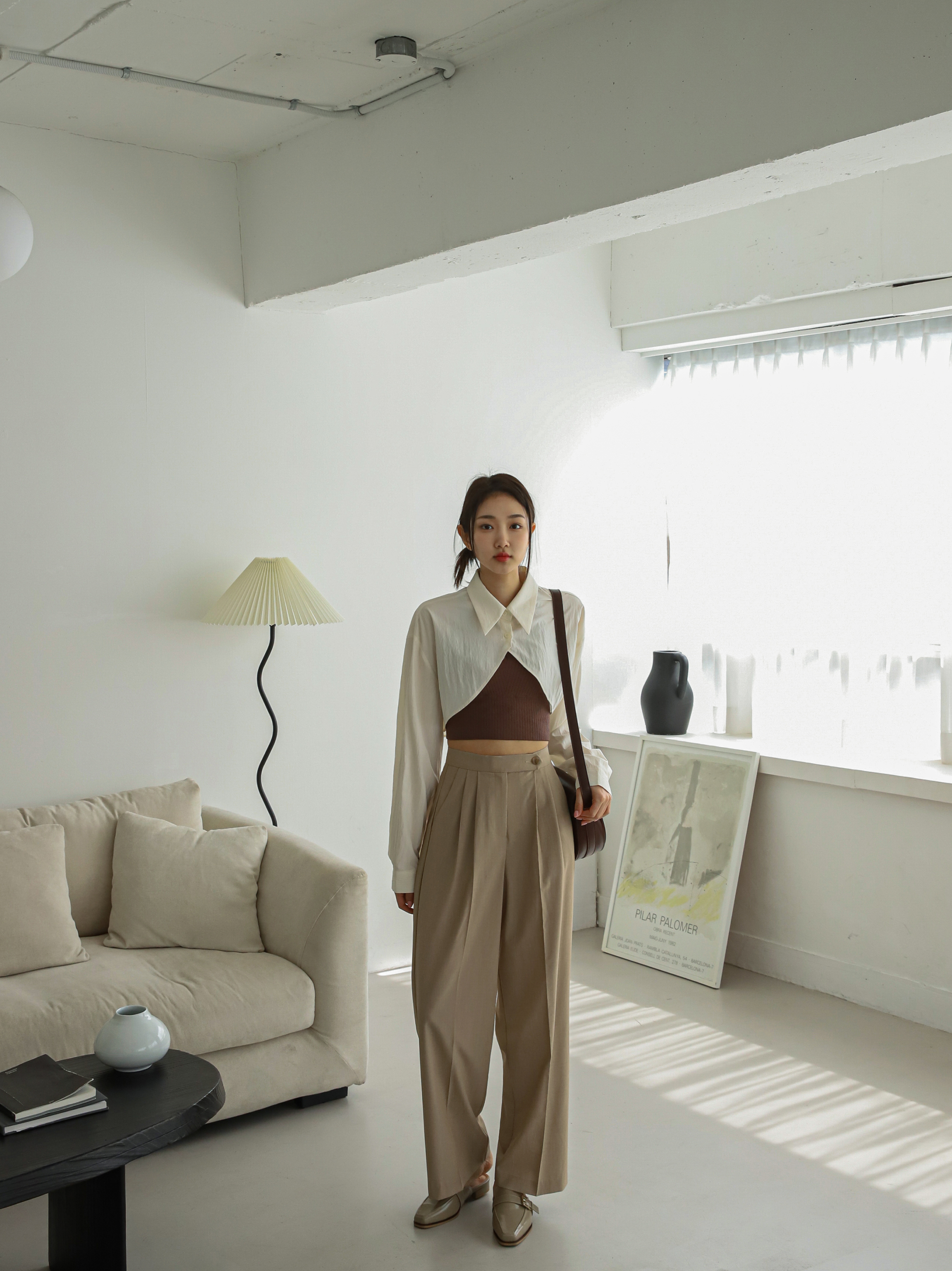 A model standing wearing a cropped collar shirt with pleated trouser.