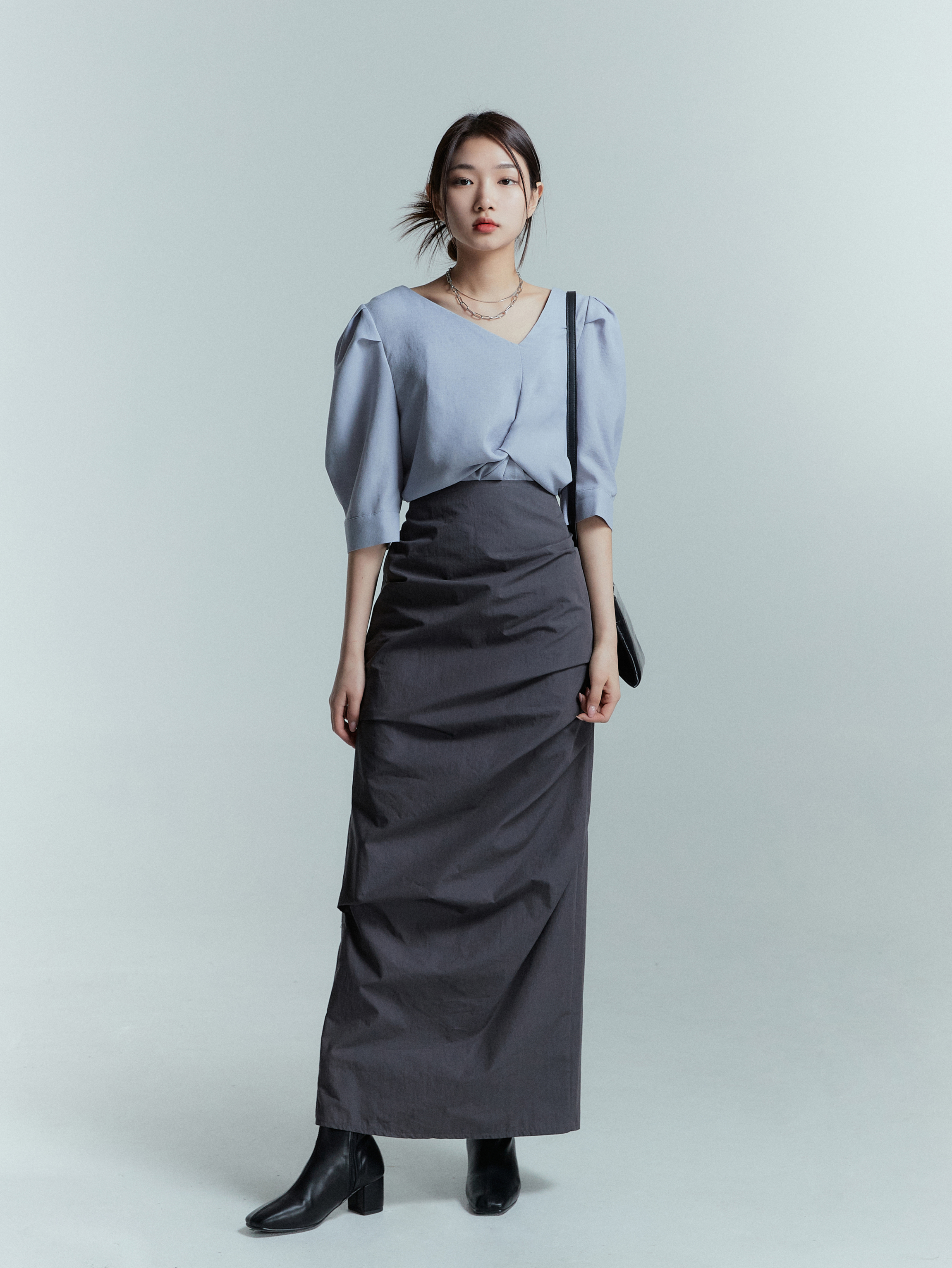 A model standing wearing a black draped skirt with gray blouse.