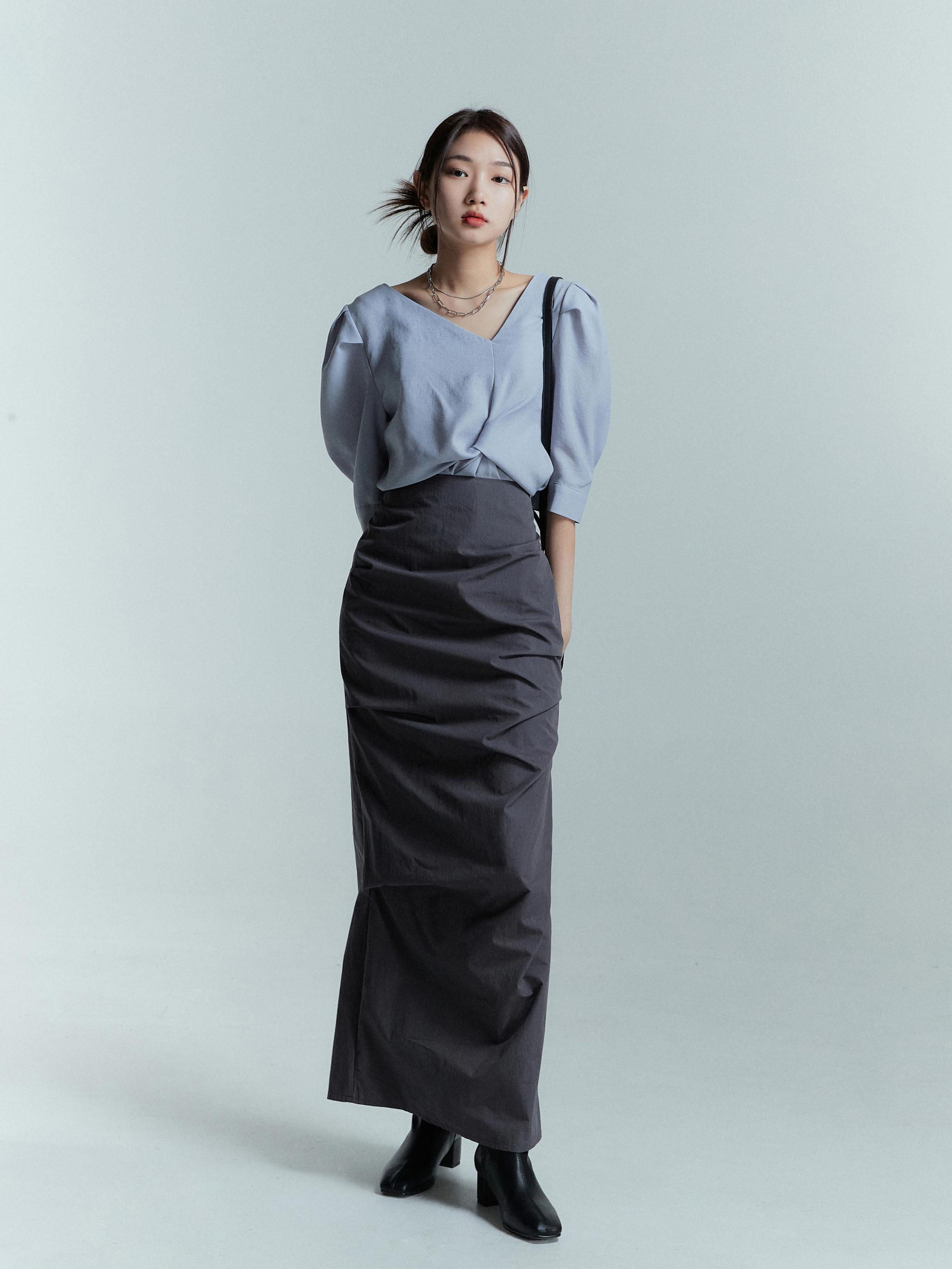 A model posing wearing a maxi draped skirt with gray blouse.