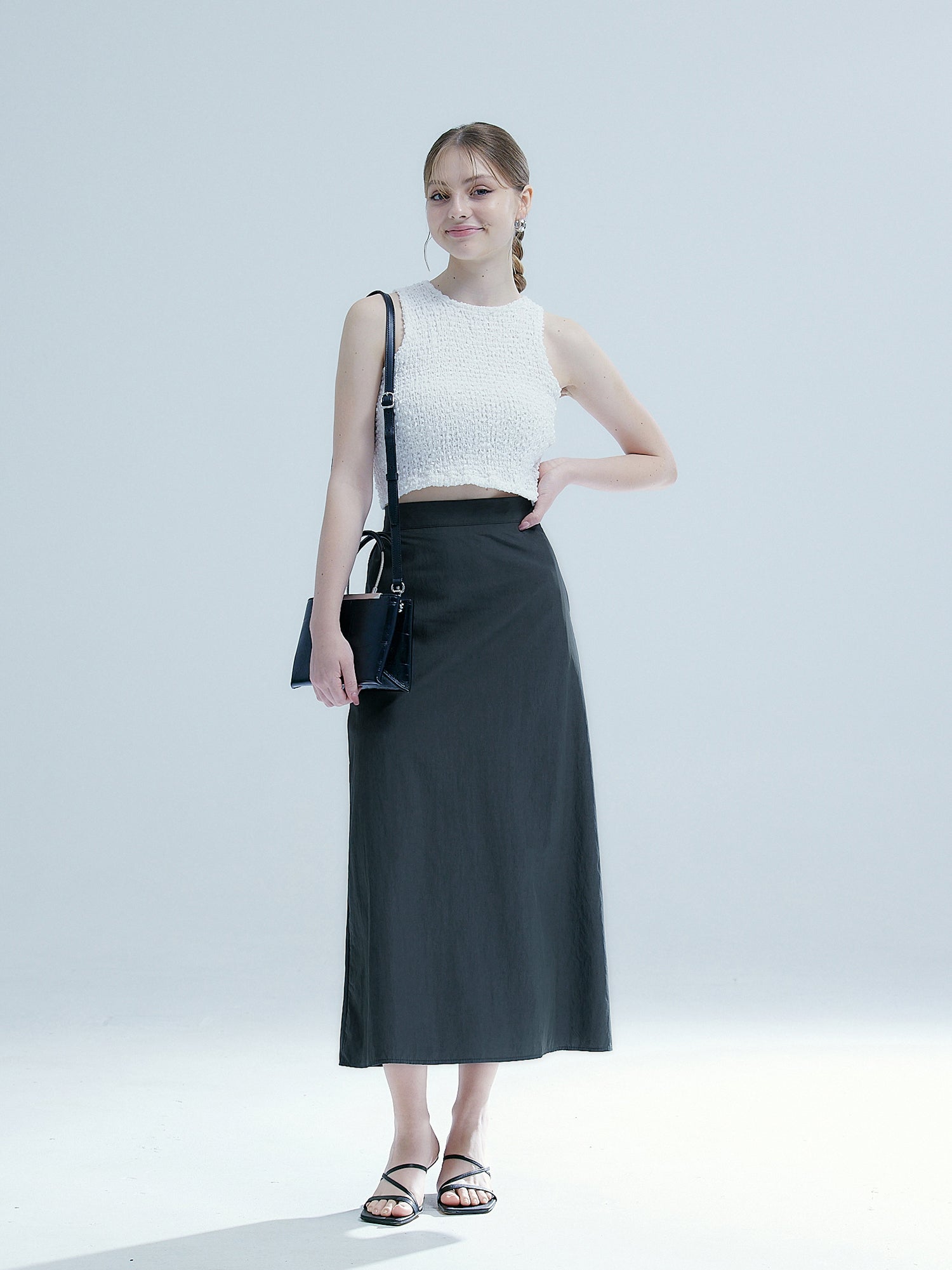 A model posing wearing the charcoal elasticated midi skirt matching it with the white textured sleeveless top. 