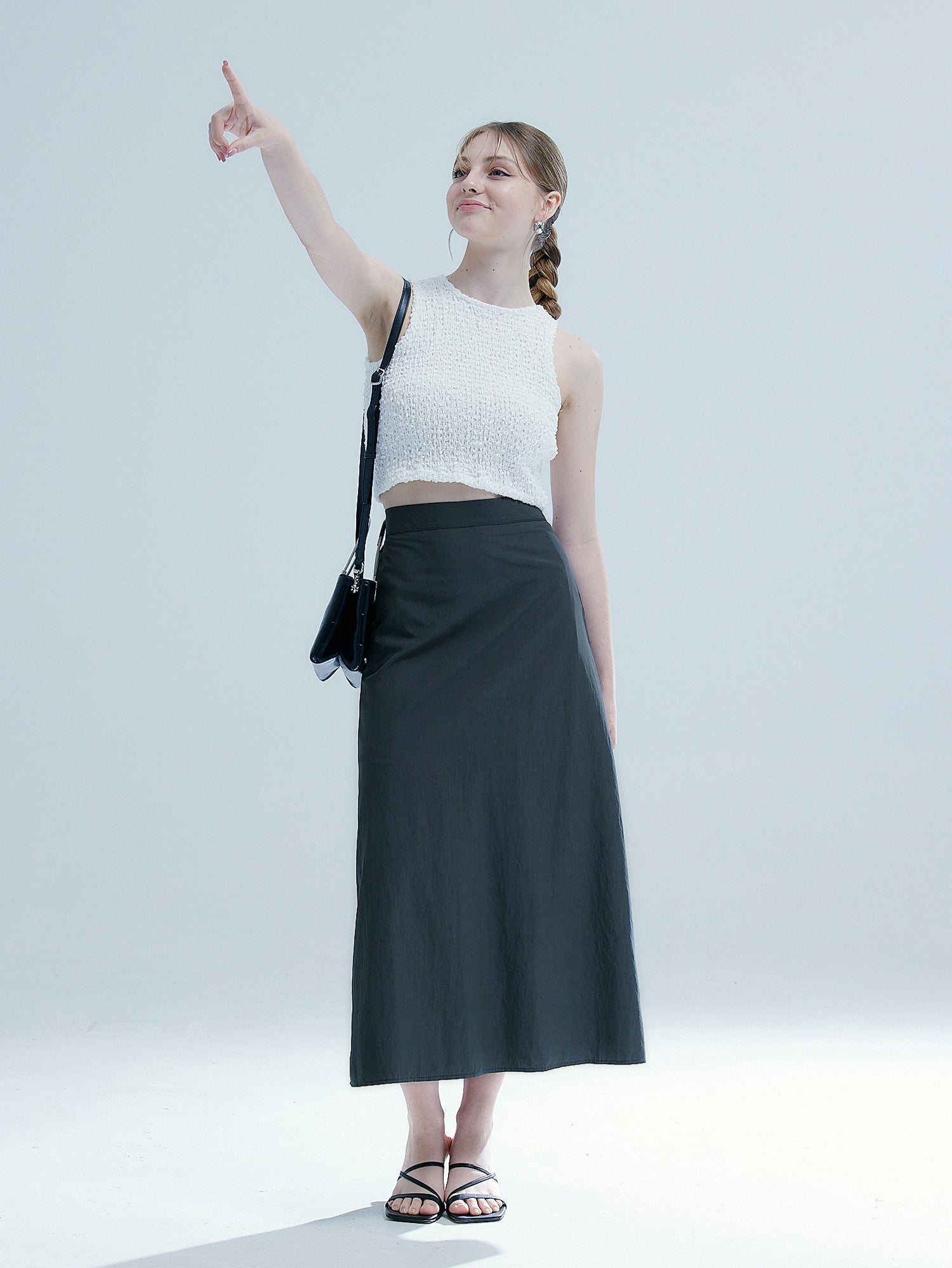 The model confidently points her finger to the sky, showcasing the charcoal elasticated midi skirt and adding a fashionable element to Korean aesthetic outfits.