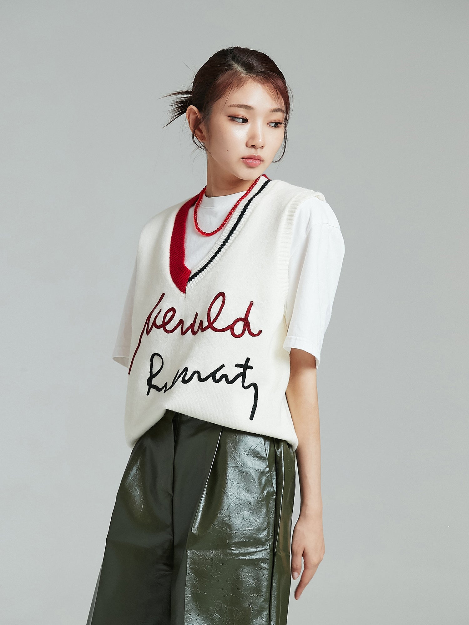 A tilted angle capturing the model's embodiment of Korean street style, showcasing the embroidered V-neck sweater vest.