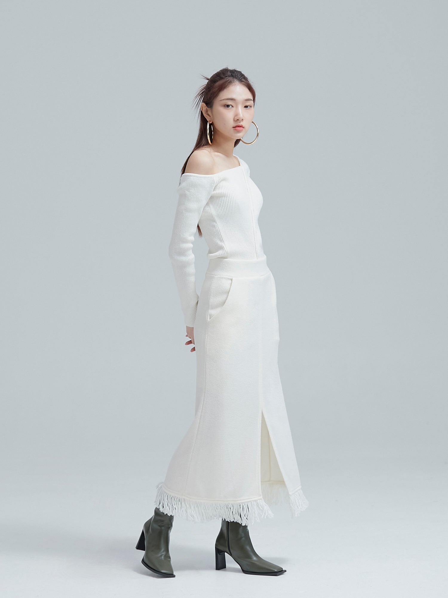 A side-angle capture featuring the model in a white fringe split maxi skirt, highlighting the intricate side designs of the garment.