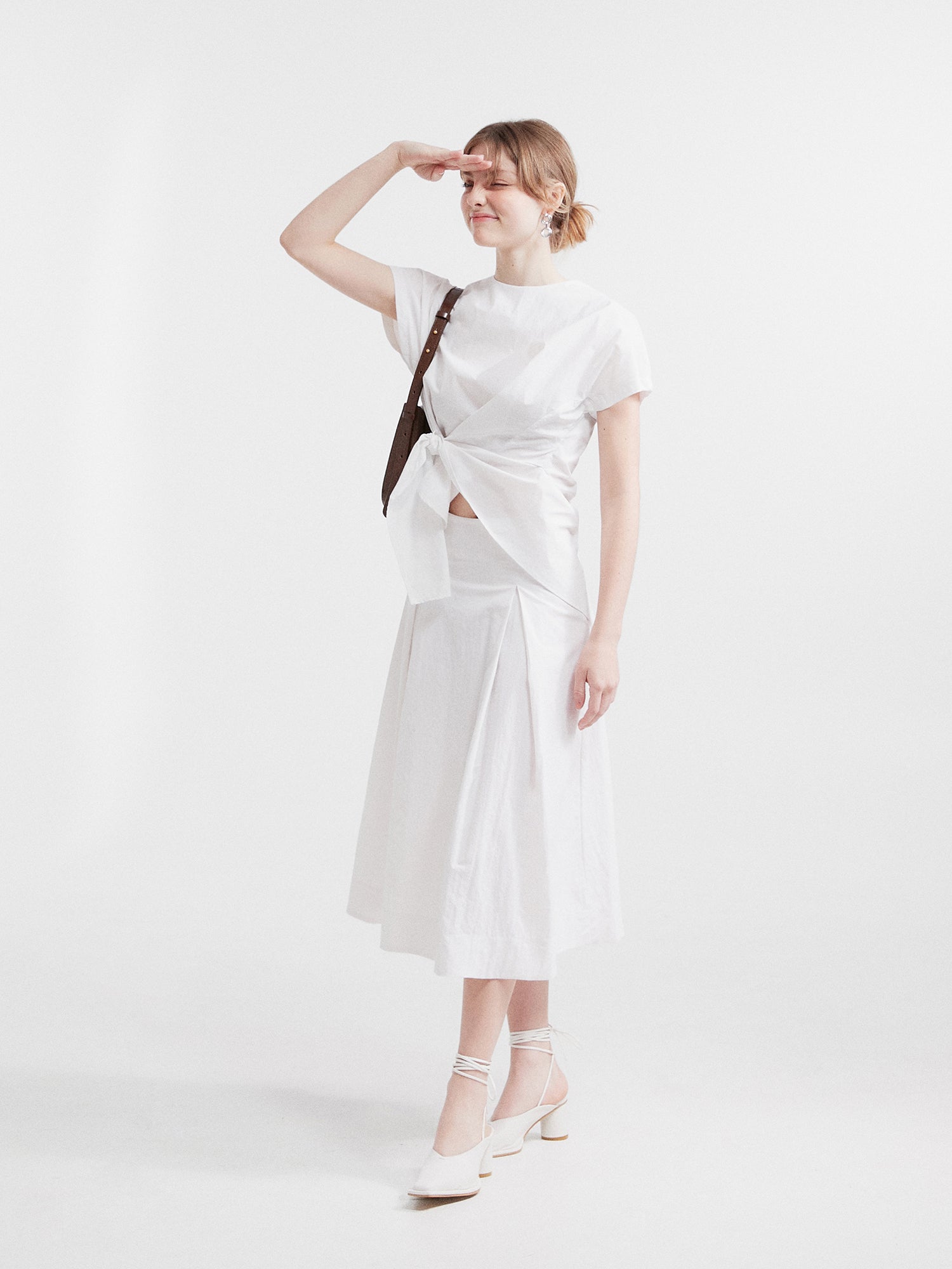 A tilted angle of a model posing wearing the ivory front wrap blouse matching it with the A-line pleated midi skirt.