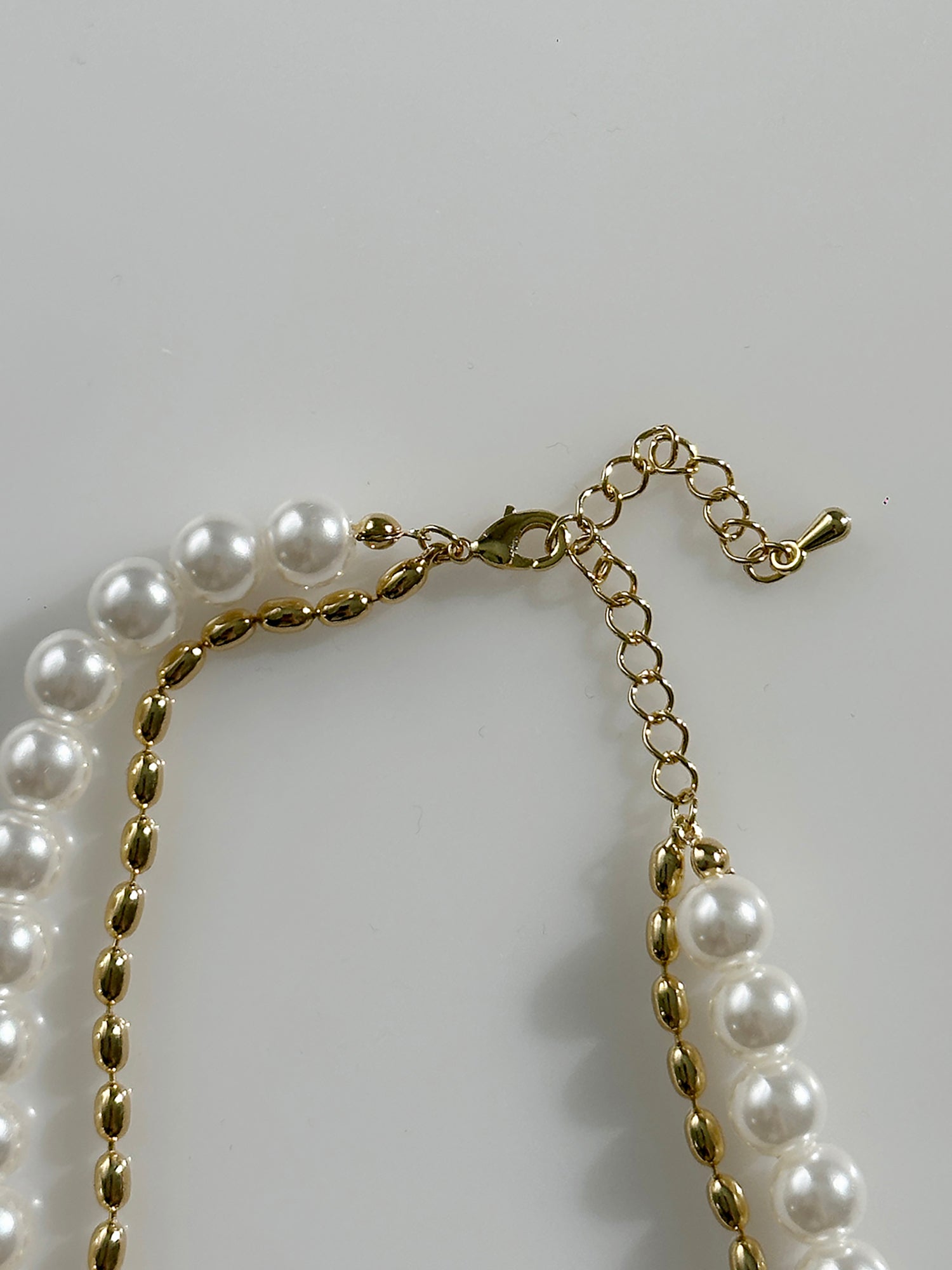 A close-up view of the gold pearl layered necklace showing the hook clasps details of the necklace.