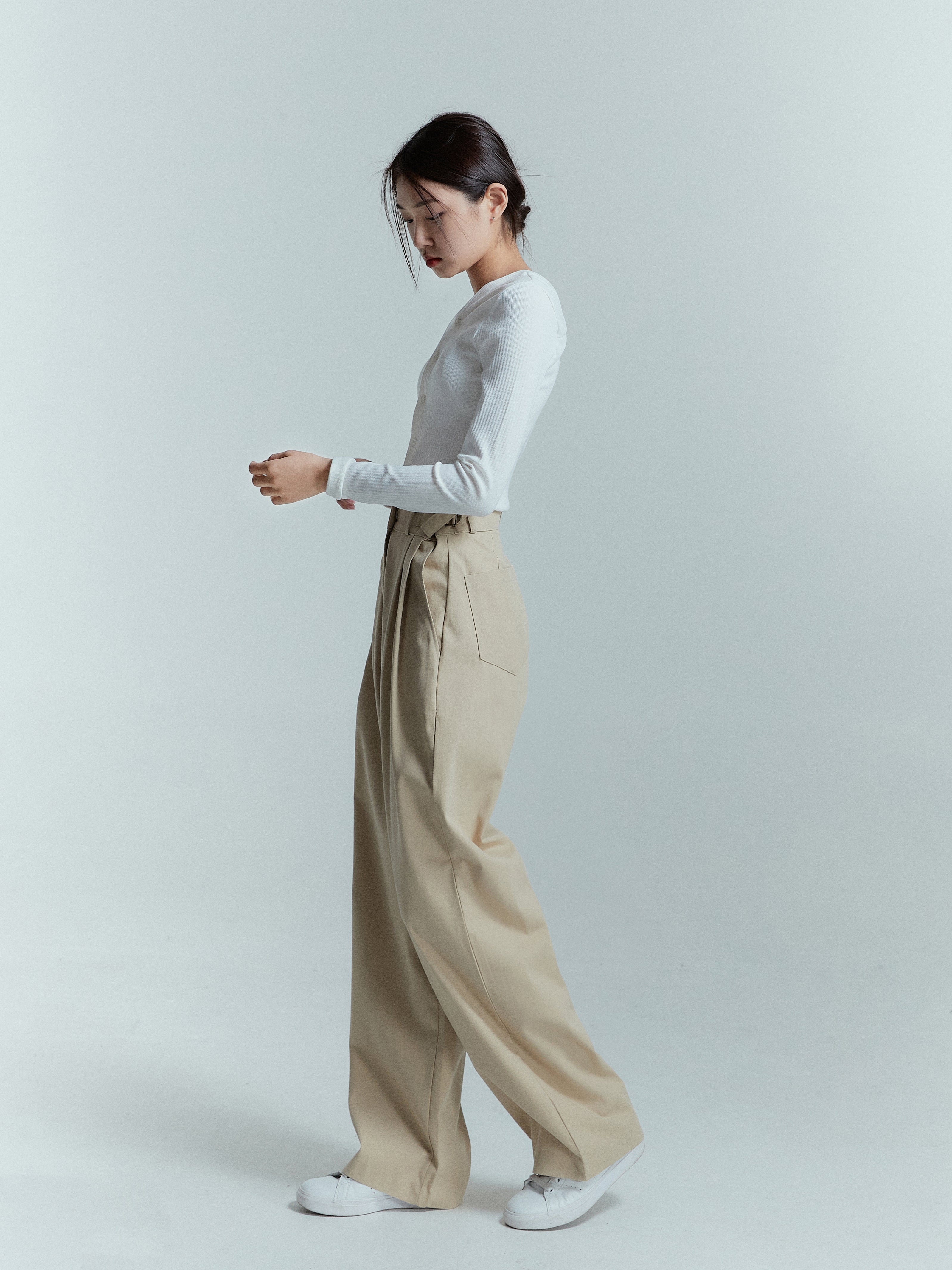 Side shot of a model wearing a cream high-pleated trouser.