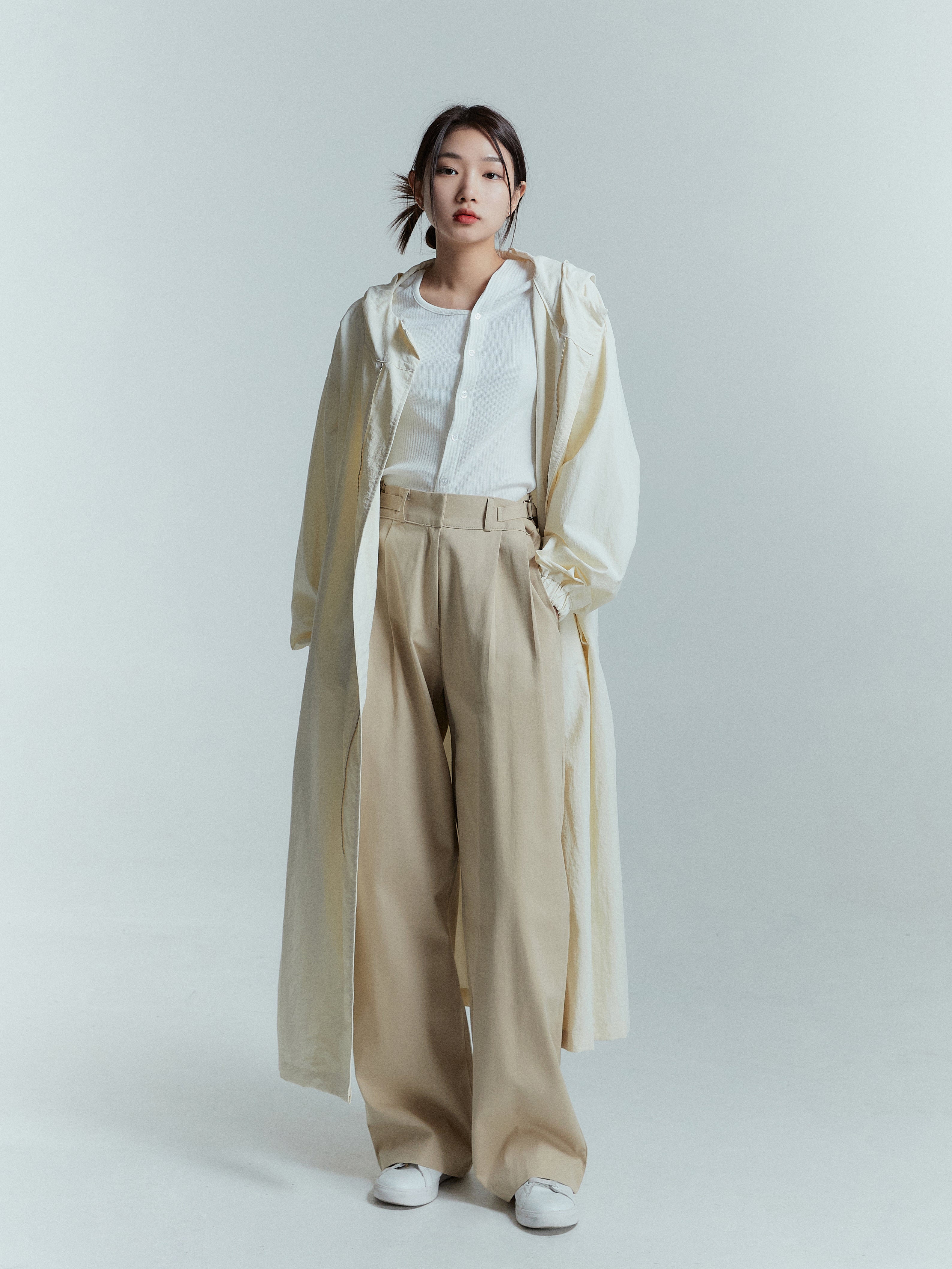 Standing pose of the model wearing the cream long coat matching it with beige high-rise trouser.