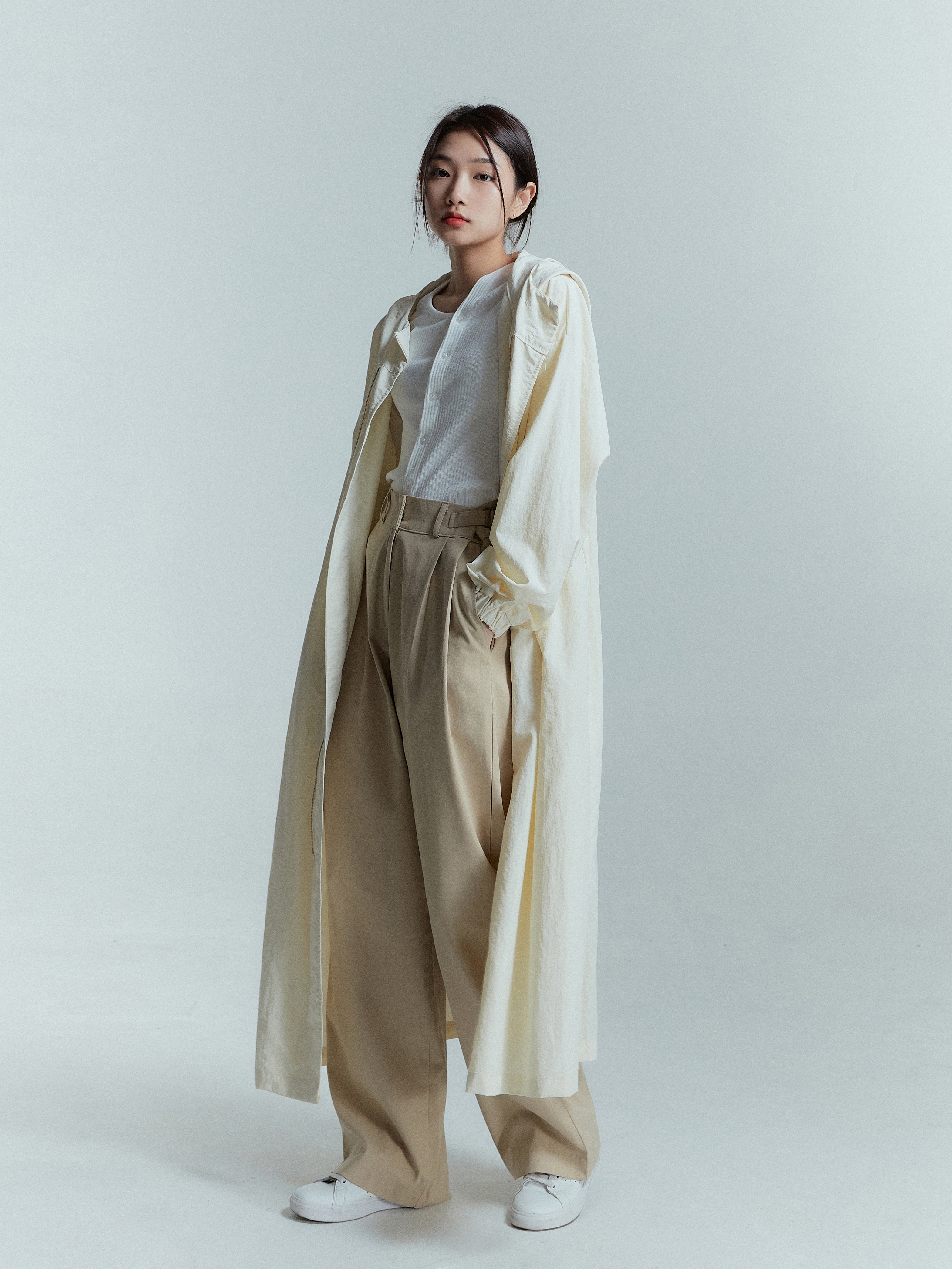 From a stylish tilted angle, the model rocks the cream hooded long coat with zippers undone, effortlessly embodying a chic and contemporary look.