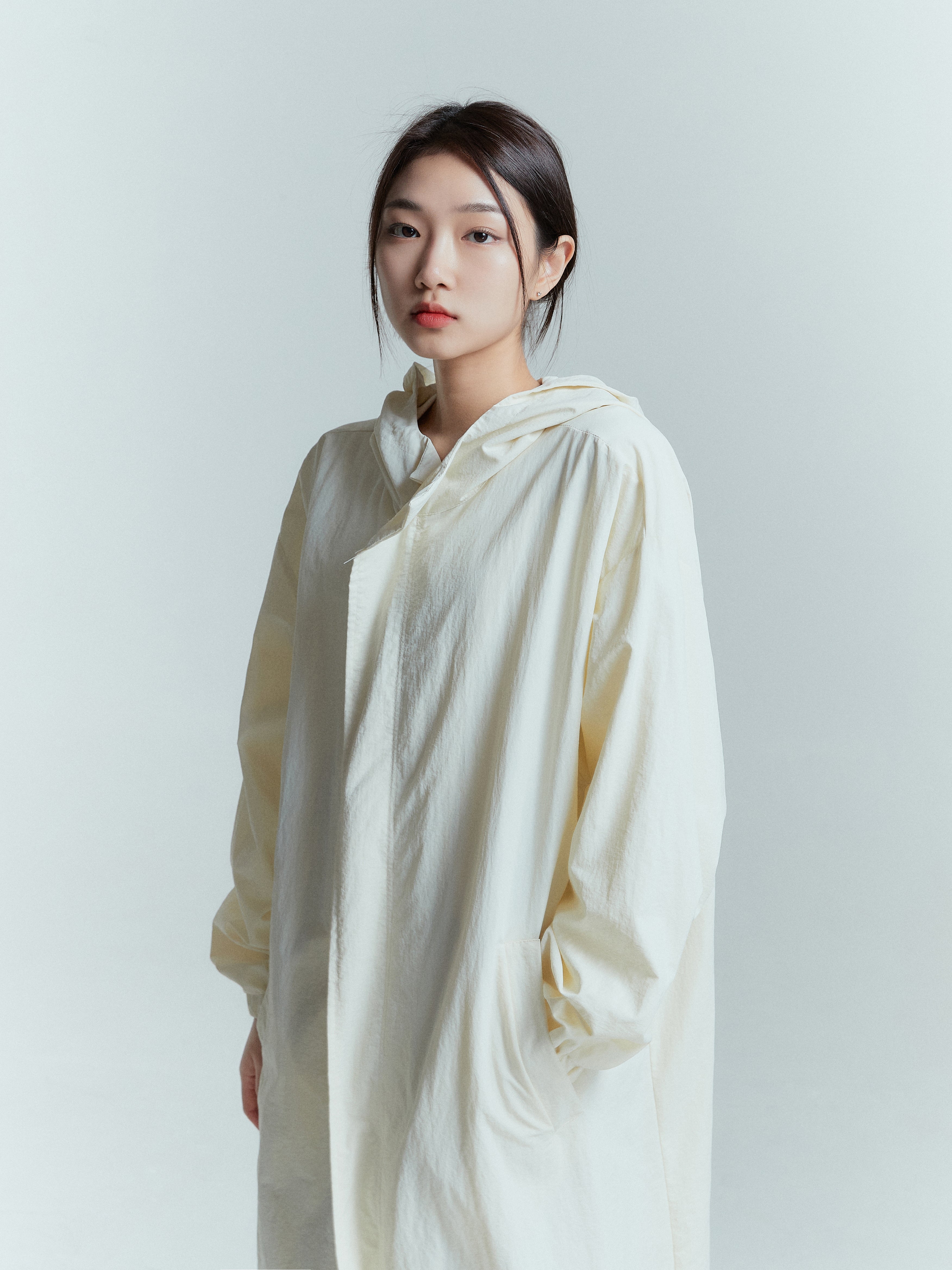 A side angle medium shot of a model wearing the ivory long coat with its zipped up.