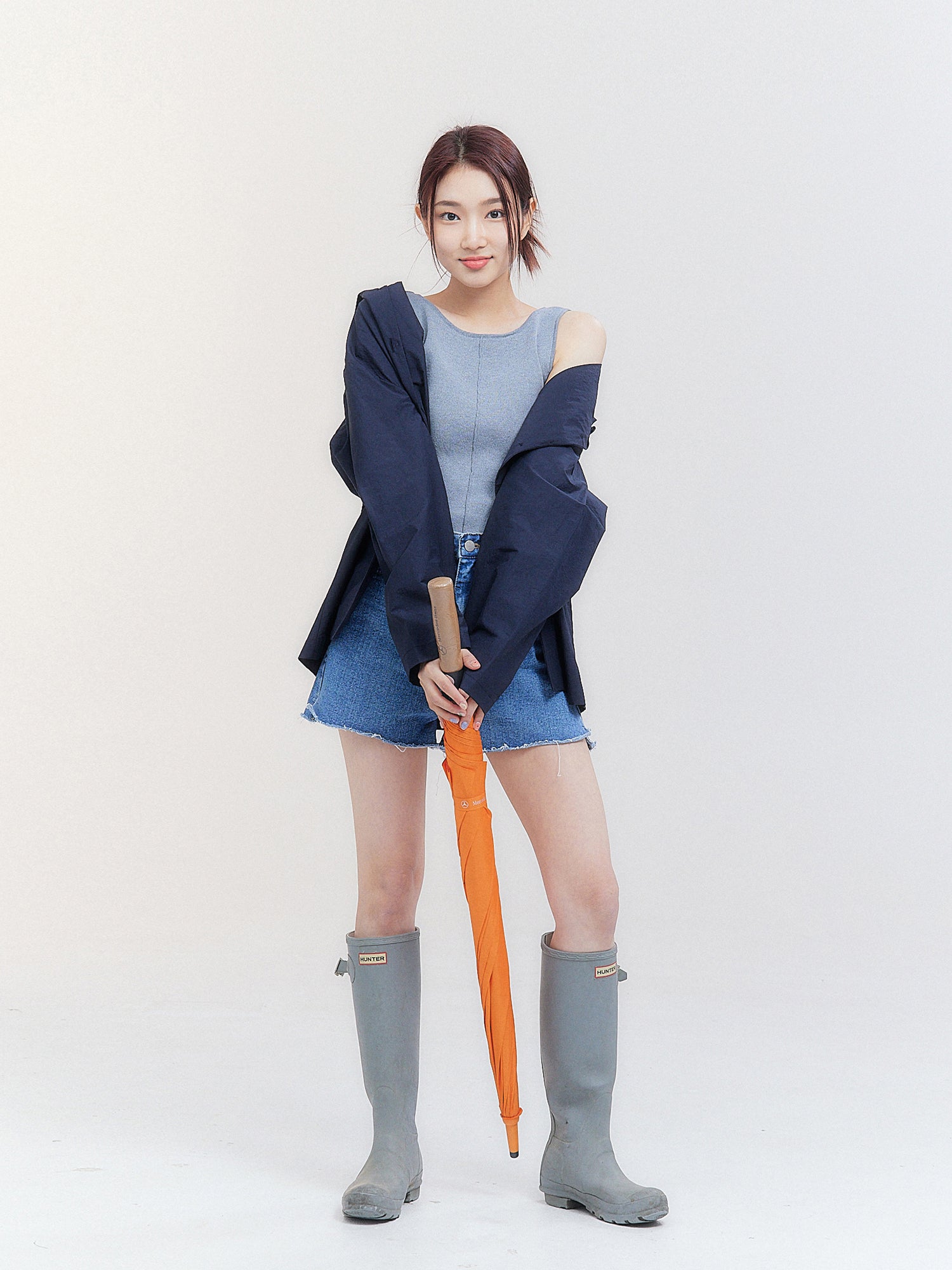 In a front-facing view that epitomizes Korean street fashion, the model strikes a striking pose, holding an umbrella while donning an open hooded raincoat.