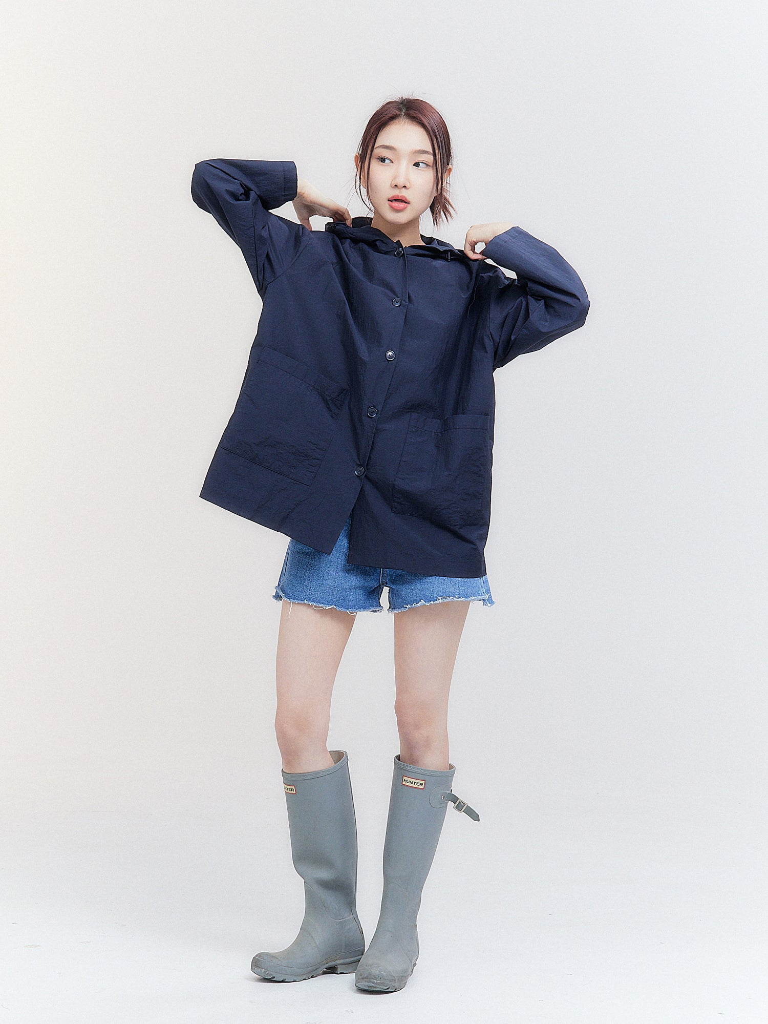 In a comprehensive shot that exudes Korean street fashion, the model showcases a fully buttoned-up hooded raincoat, highlighting its snug fit and trendy appeal.