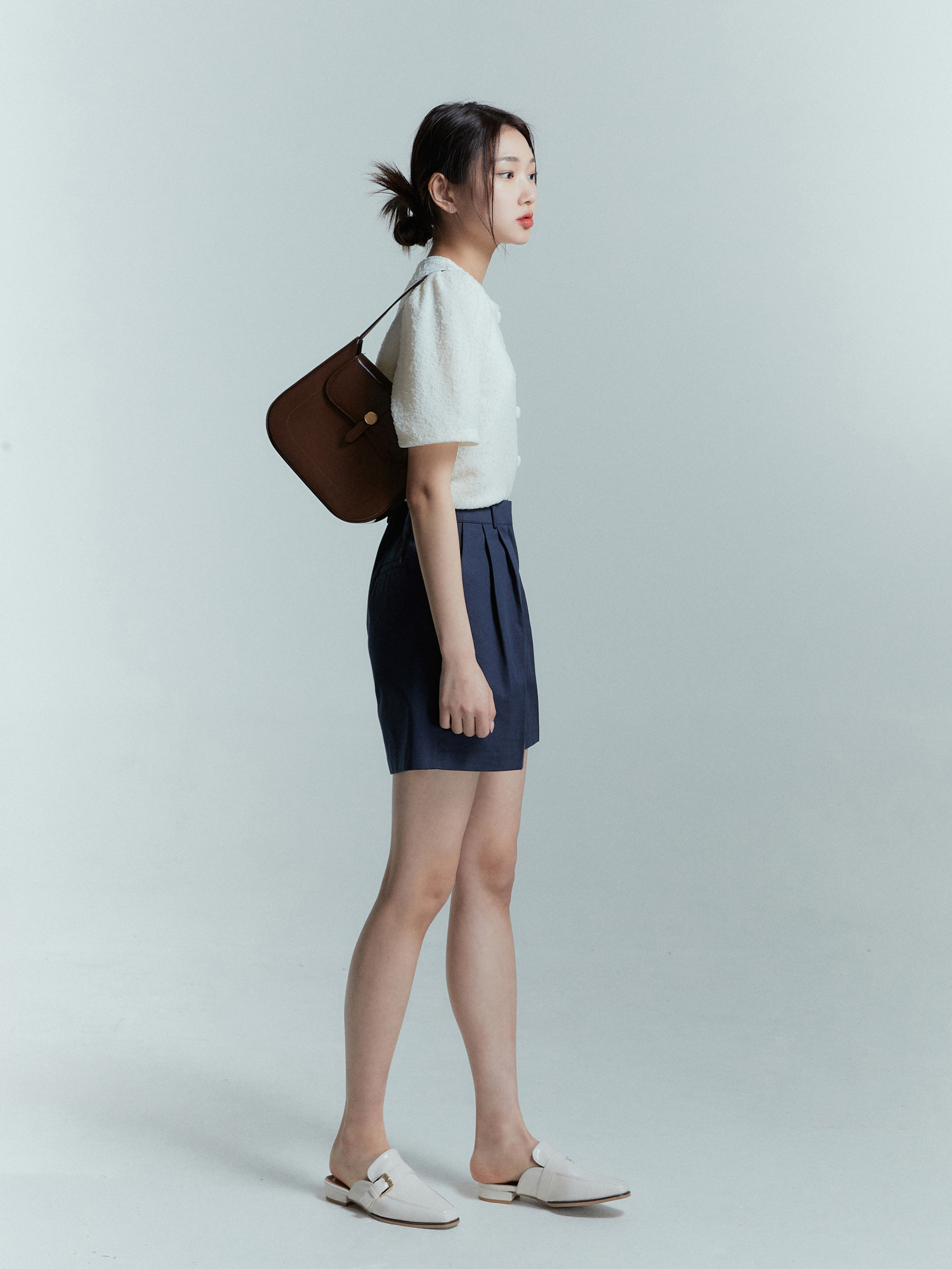 A side angle of a model wearing the ivory knit cardigan matching with navy shorts.