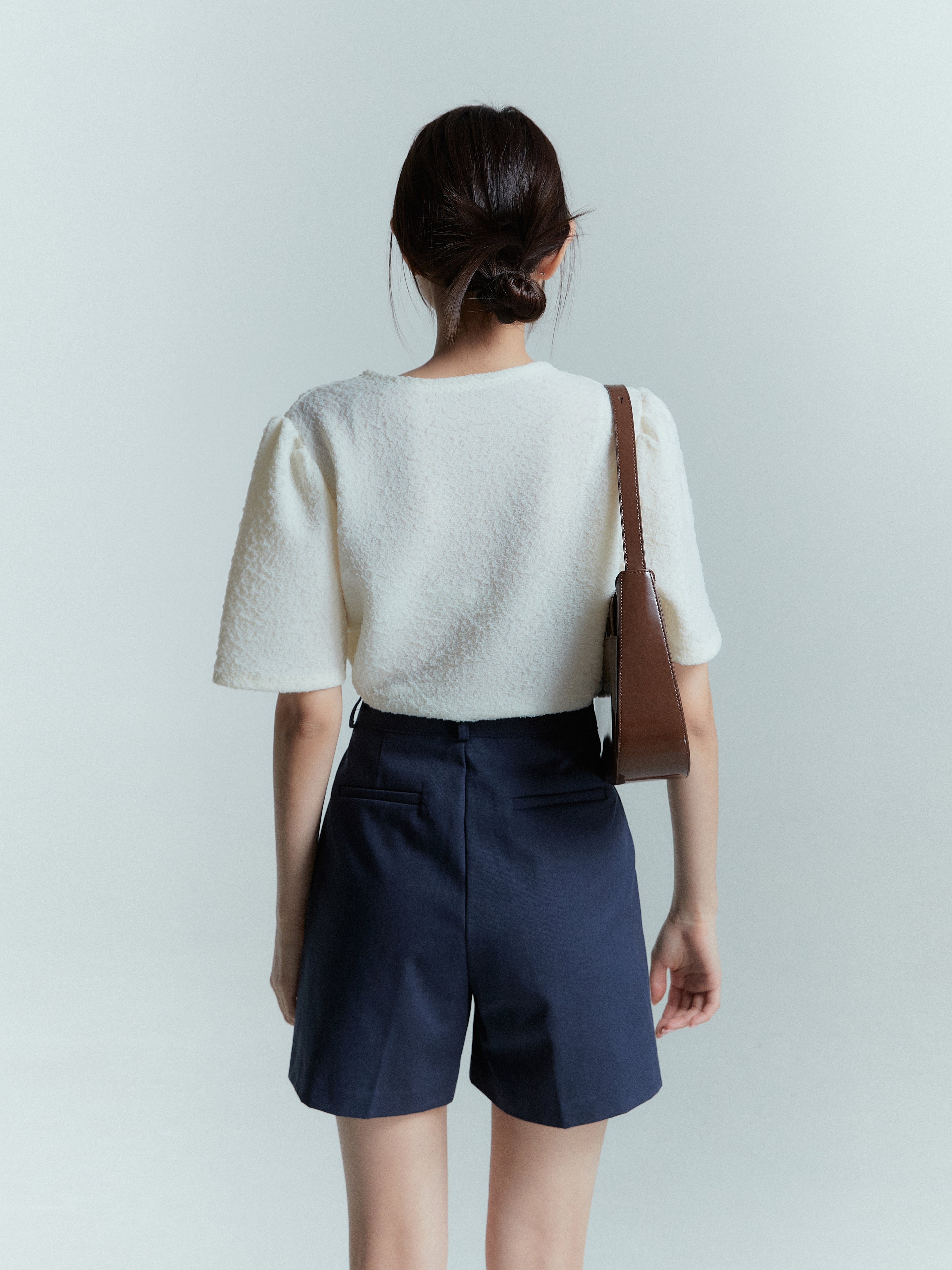 Back view of a model showcasing the backside of the pleated trouser shorts, featuring the back pockets and stitching.