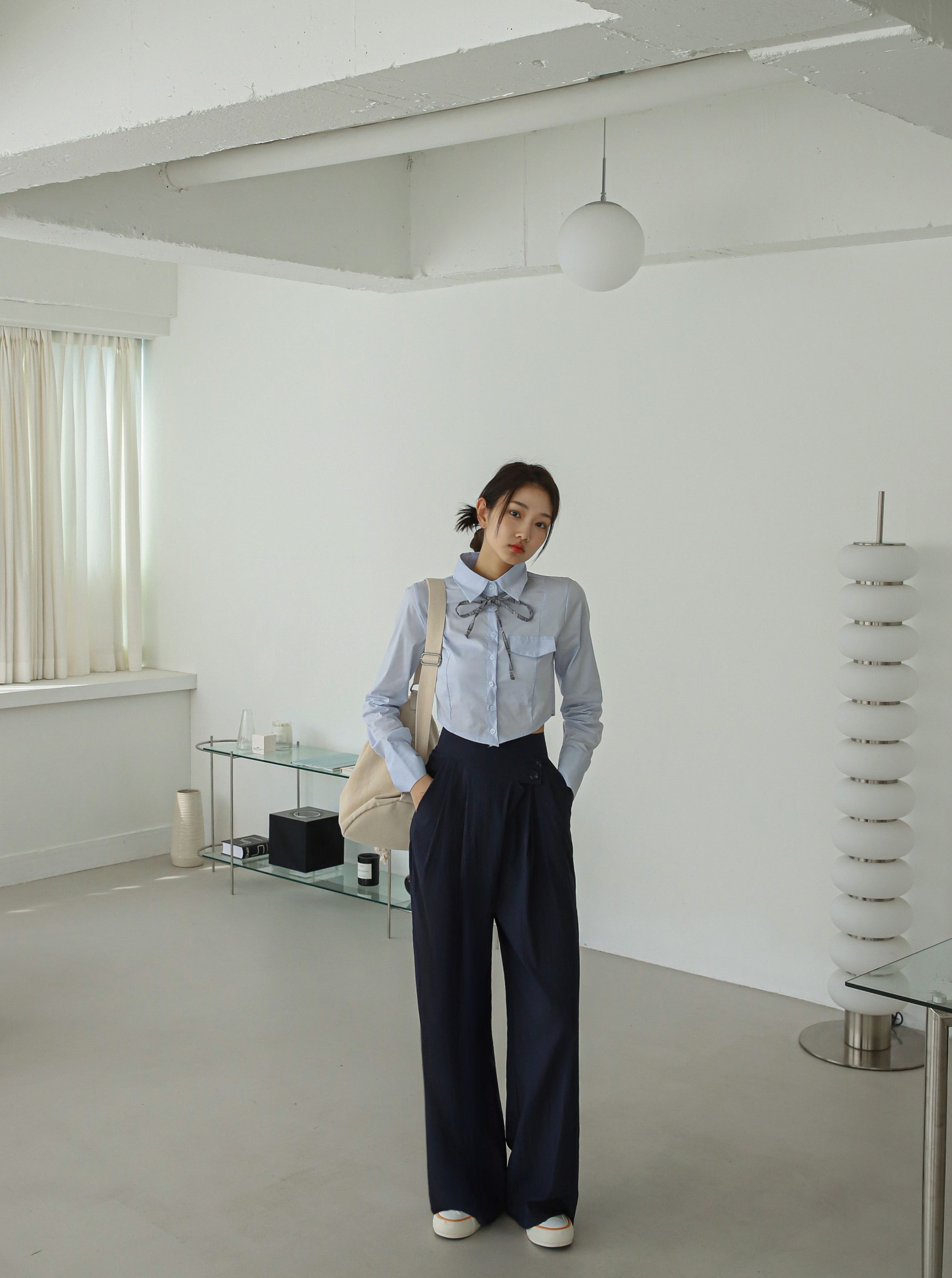 A full shot of a model wearing a laced collar shirt with pleated trouser pants.