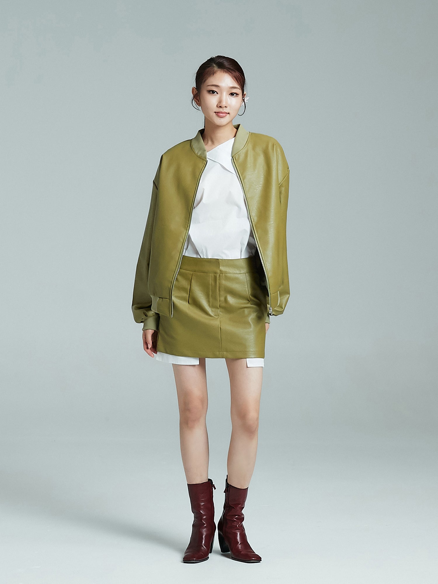 Full shot of the model wearing the set of leather bomber jacket and mini leather skirt to showcase its chic korean street fashion vibe.