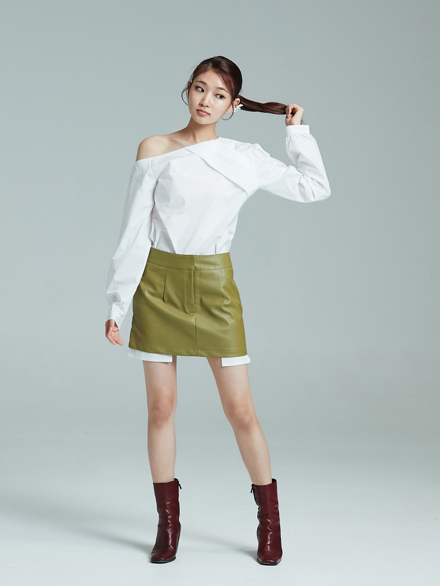 A full-length photograph of the model elegantly adorned in a one-shoulder blouse, perfectly coordinated with a leather mini skirt.