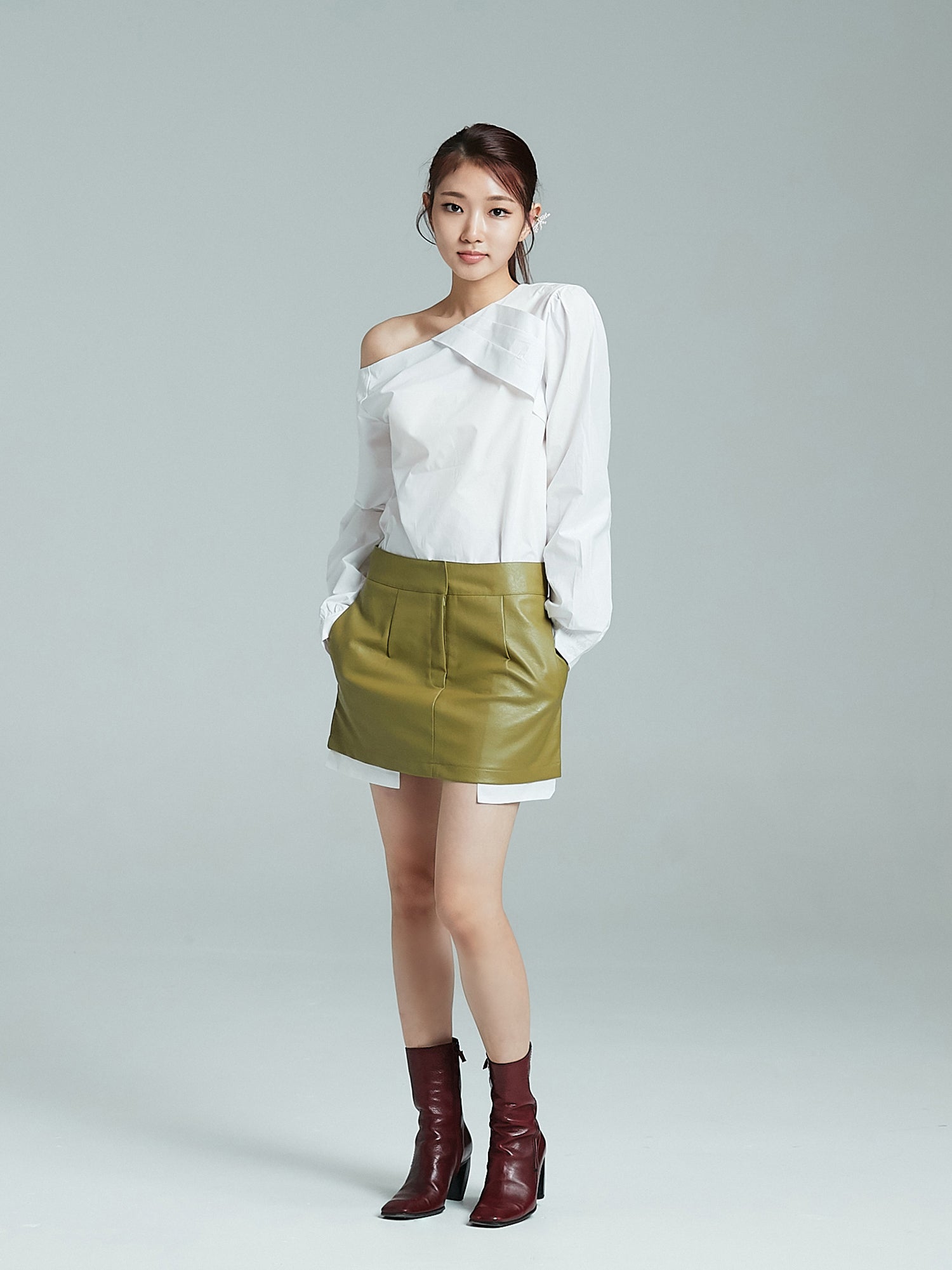 Front look of the one shoulder blouse with her hands tucked inside the leather mini skirt.