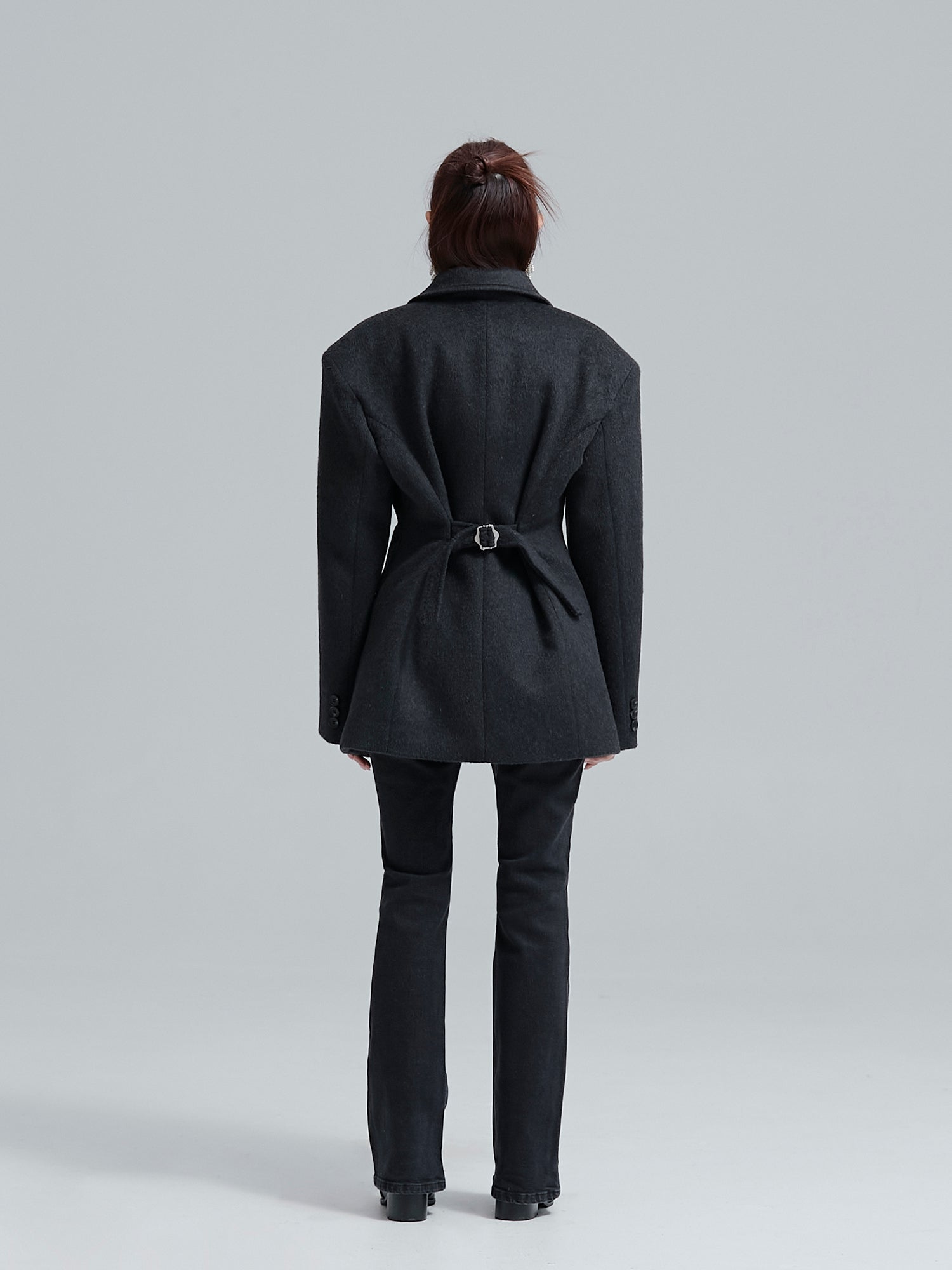 Back shot of the model wearing the padded fitted coat highlighting its adjustable back belt.