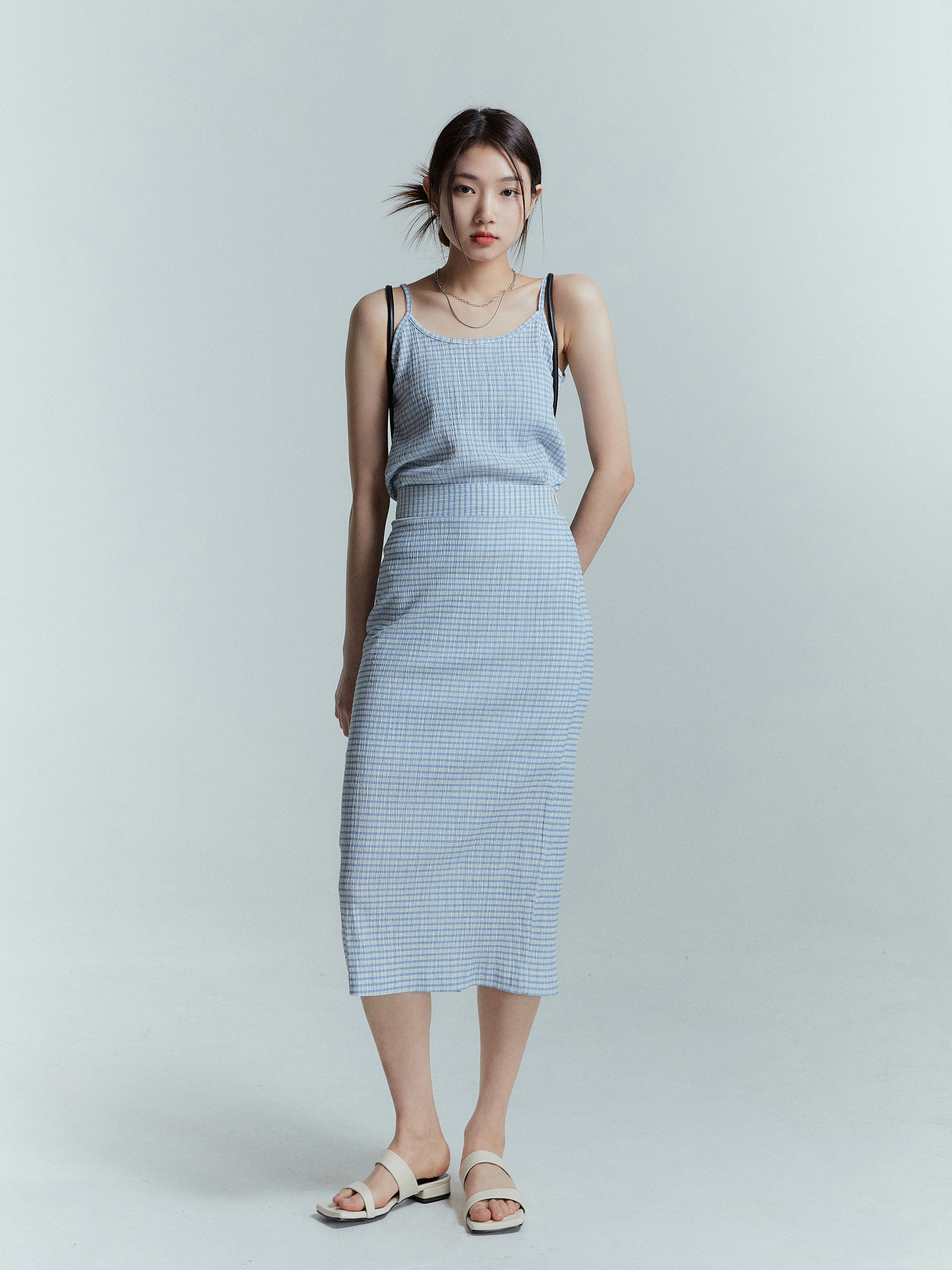 A model stands confidently, wearing a plaid midi skirt paired with a matching tank top, exuding a summer vibe.