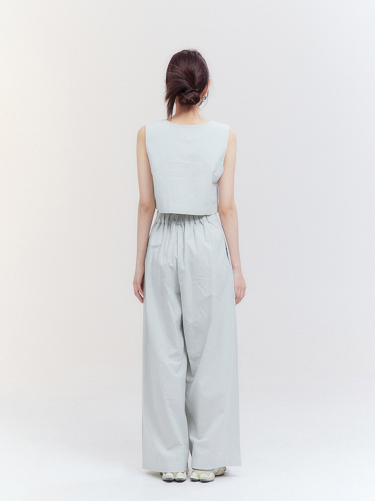 A back view of the model wearing the pleated slit skirt pants, highlighting the impeccable back fitting of the garment and embodying the essence of Korean street fashion.