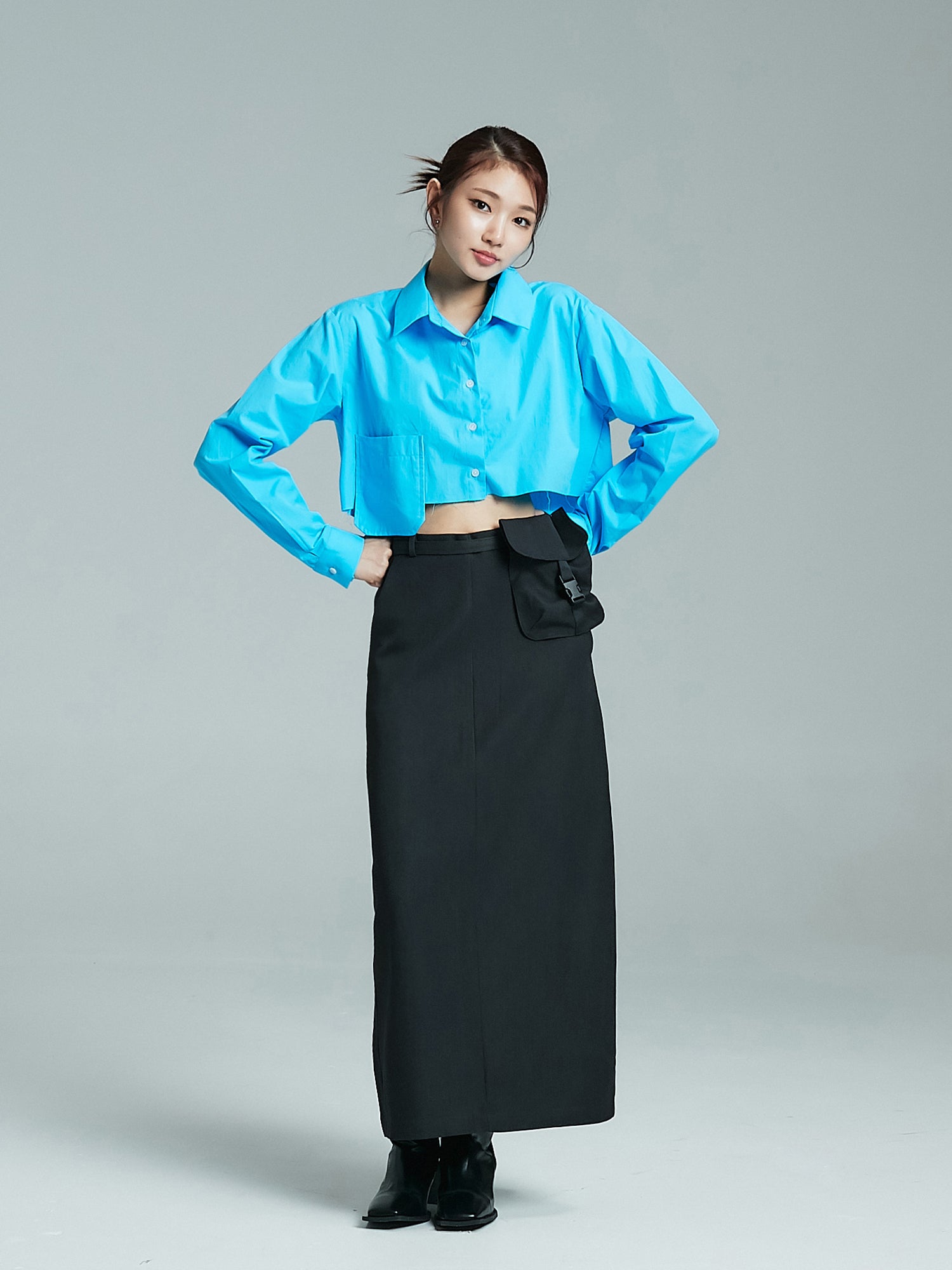 A full-length shot featuring the model wearing the blue pocketed cropped shirt, showcasing the shirt's complete and flattering fit.