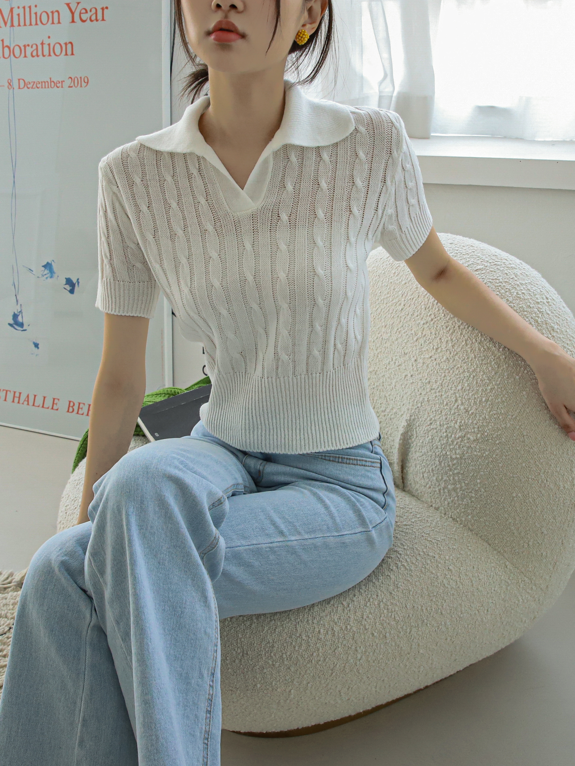 A model in a seated position wearing the ivory polo knit shirt.