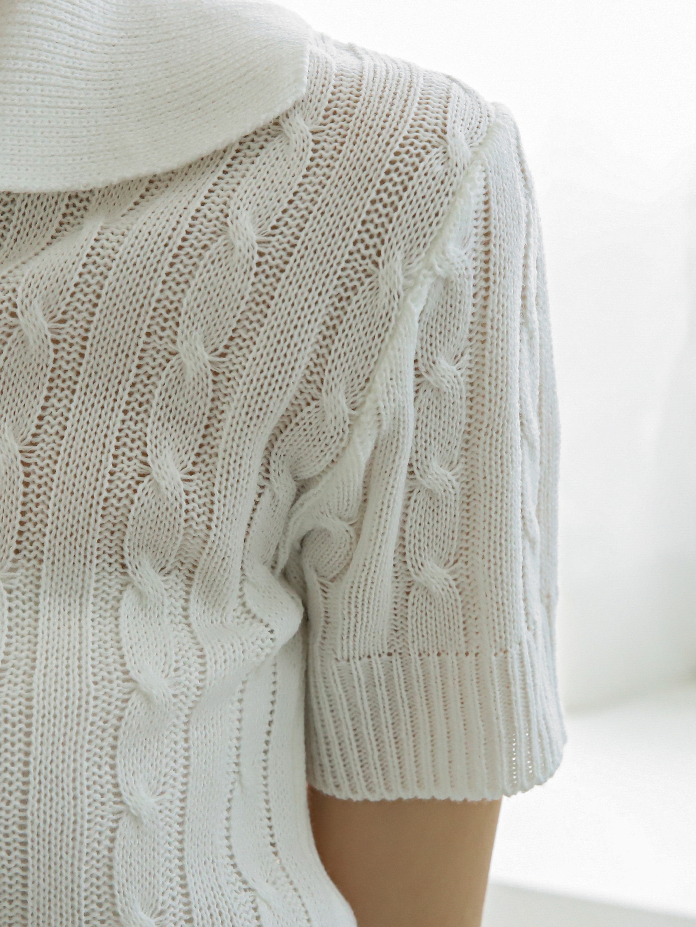 A zoomed-in shot of the ivory knit shirt showcasing the cable knit patter and the sleeve details.