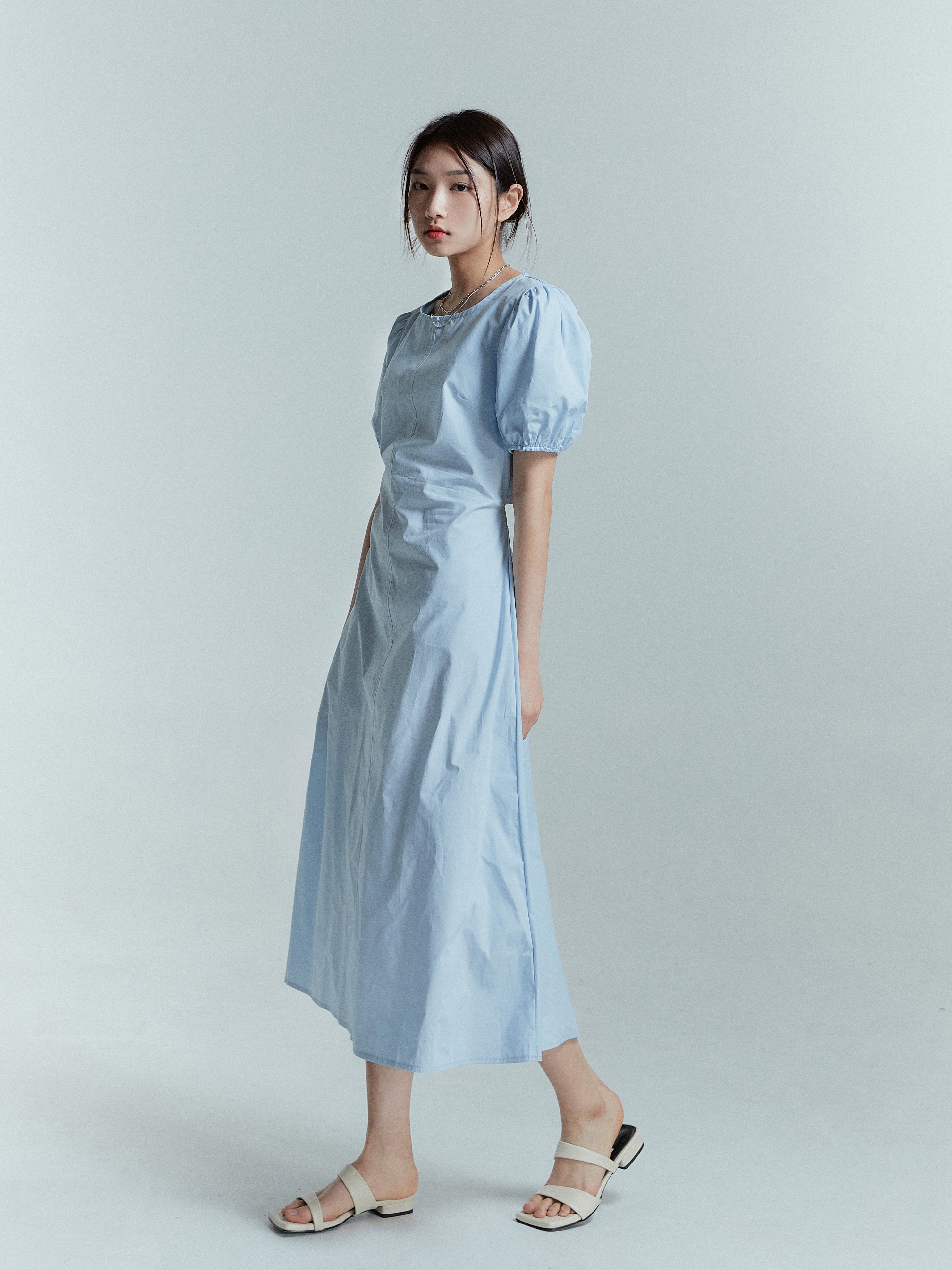 A side angle of a model wearing the light blue puff sleeve dress styled with beige sandals.