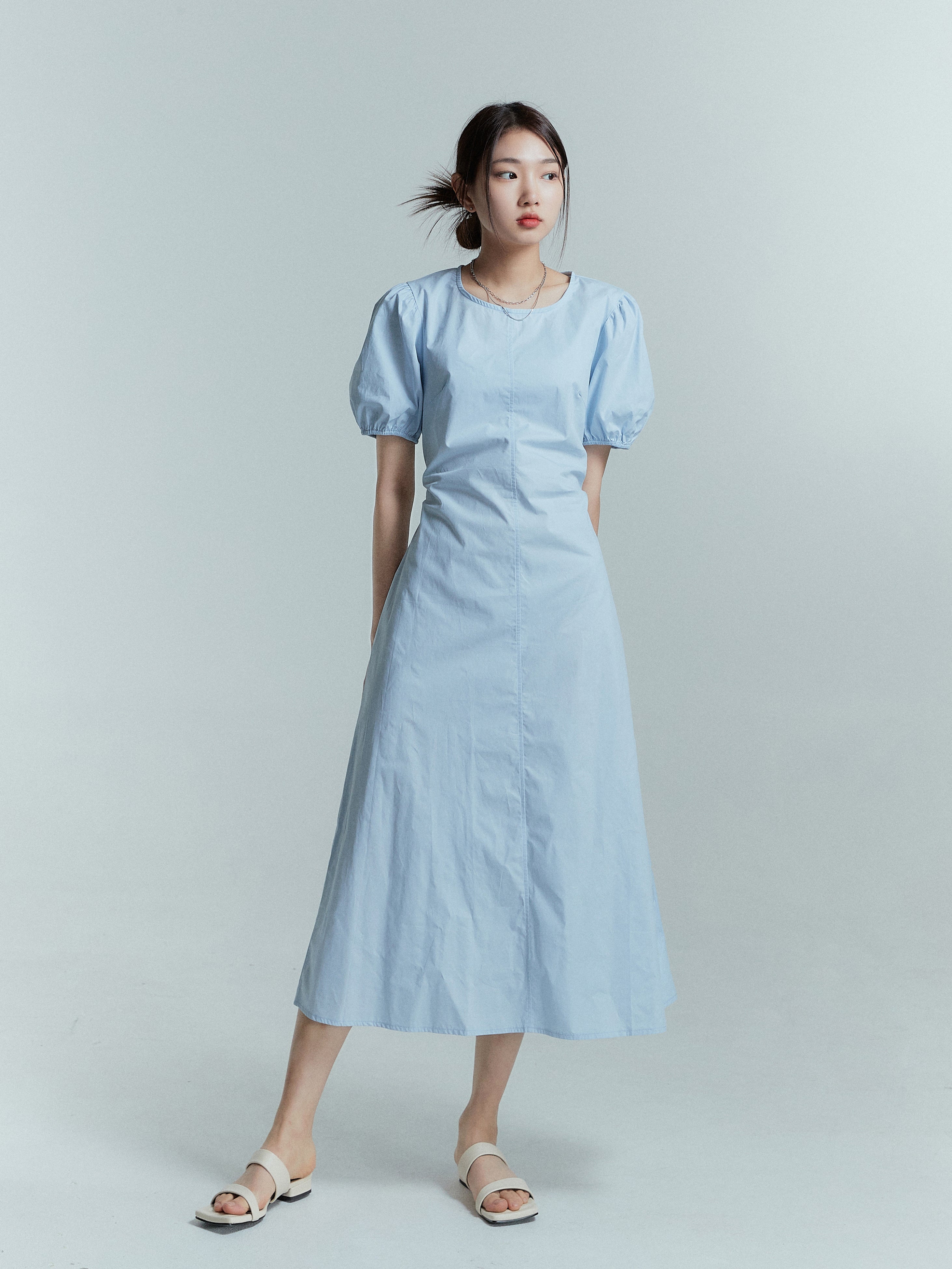 Captured in a straight stance, the model glances to the side, showcasing the full-length of the puff sleeve dress.