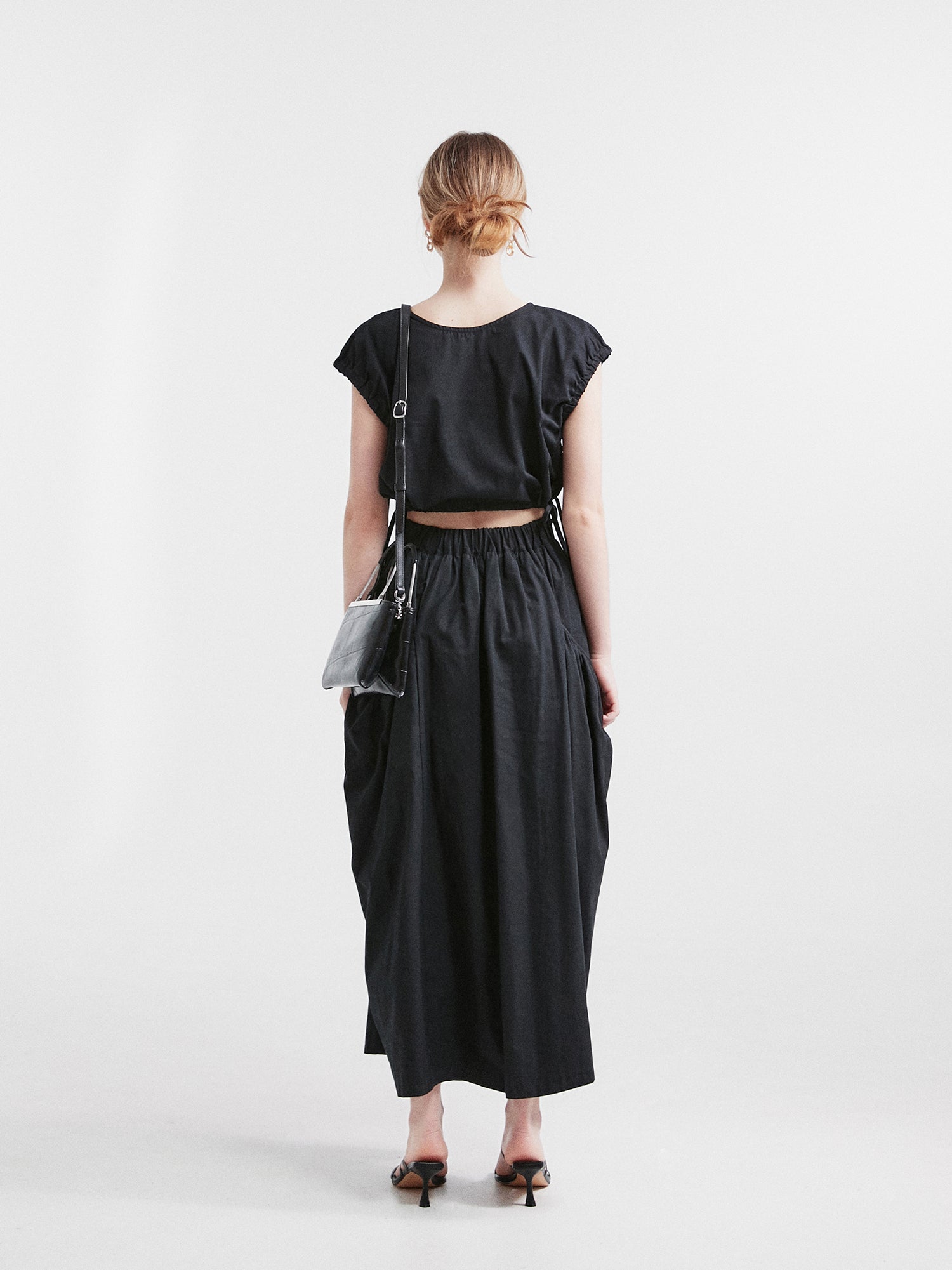 A back view of a model wearing the elastic waist midi skirt highlighting the elastic waist of the skirt.