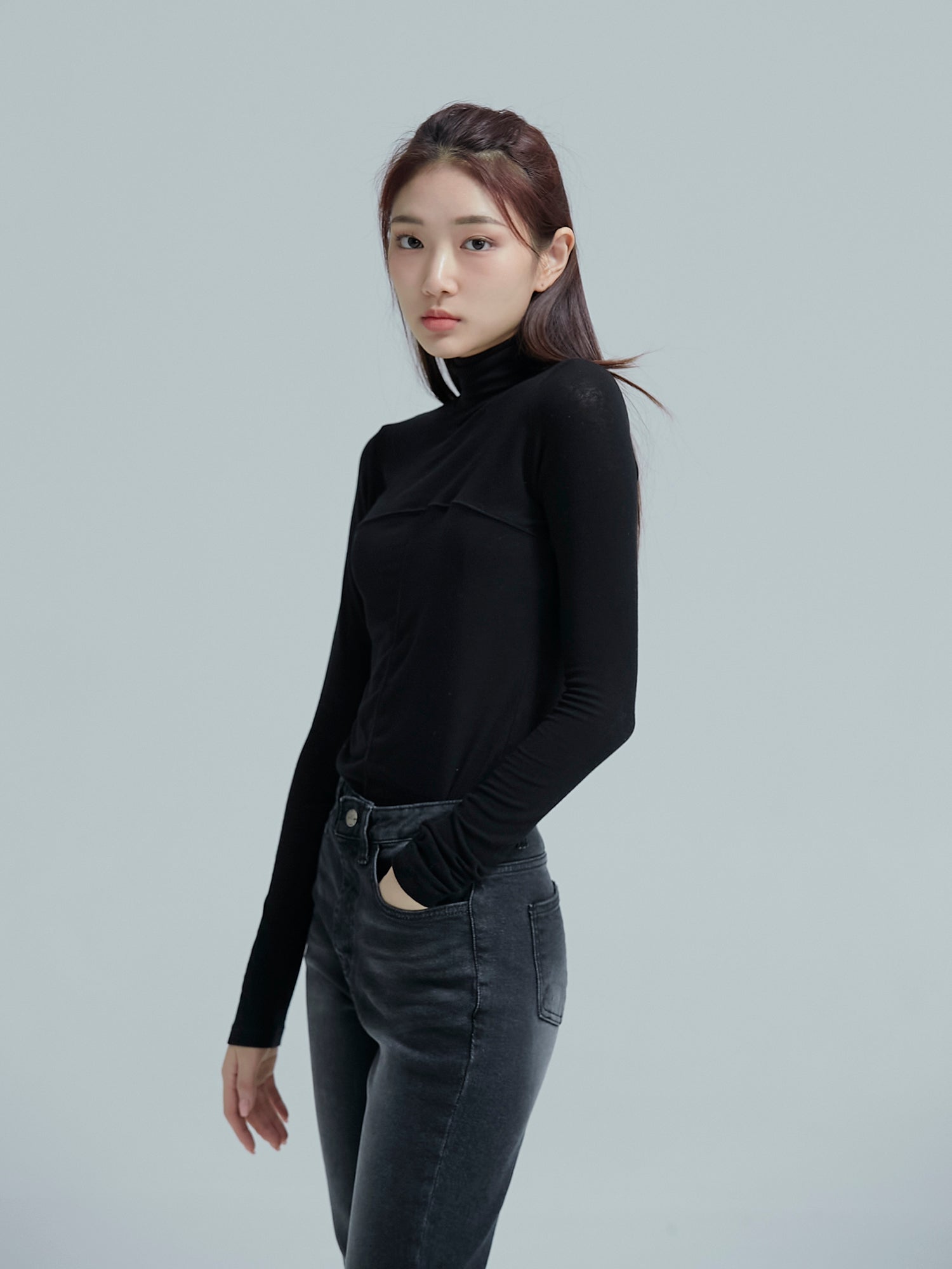 A tilted view of the model wearing the seamed turtleneck showing its side fitting of the turtleneck.