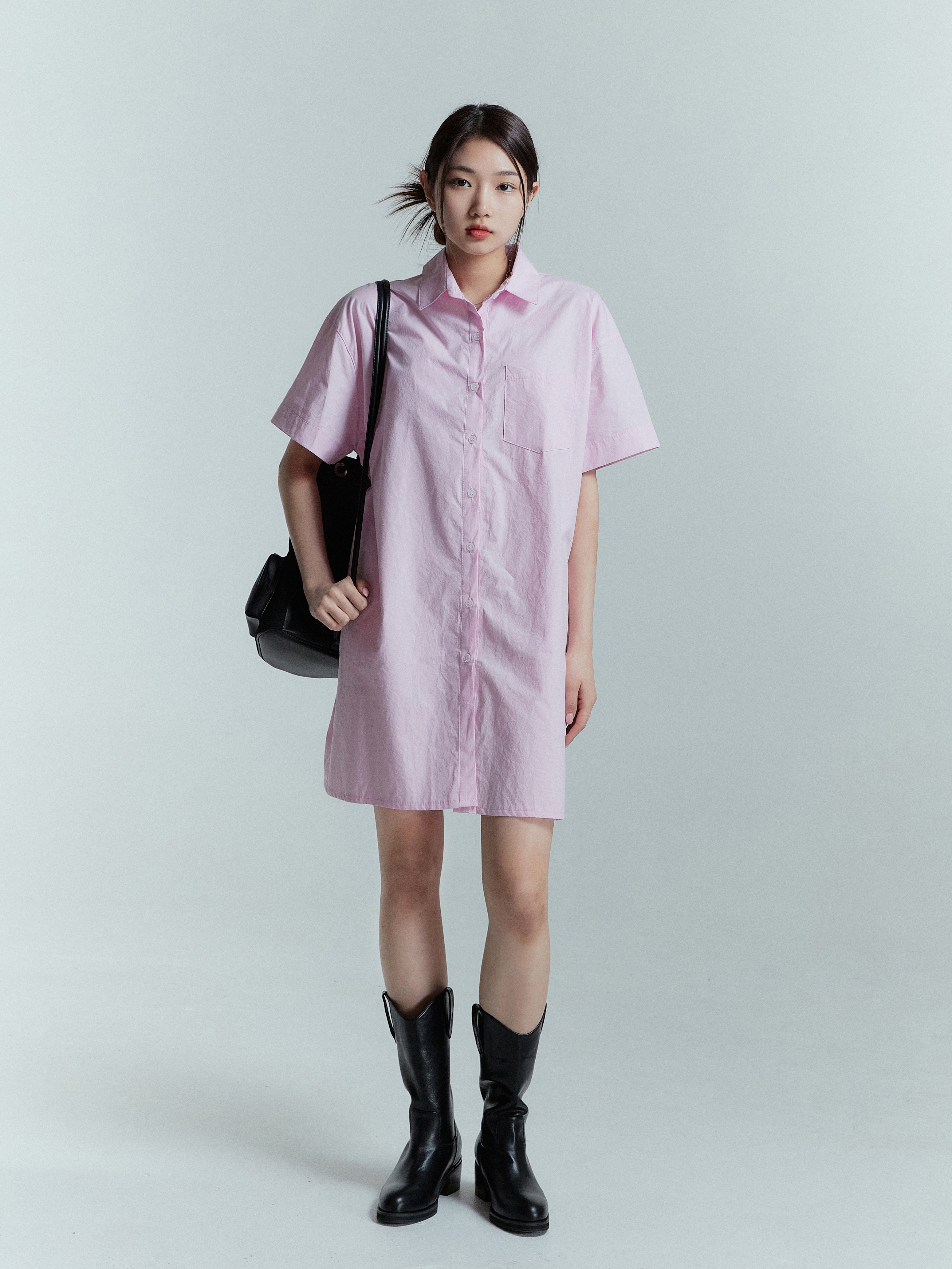 Standing model shot wearing the pink shirt dress perfectly complimenting it with black boots.