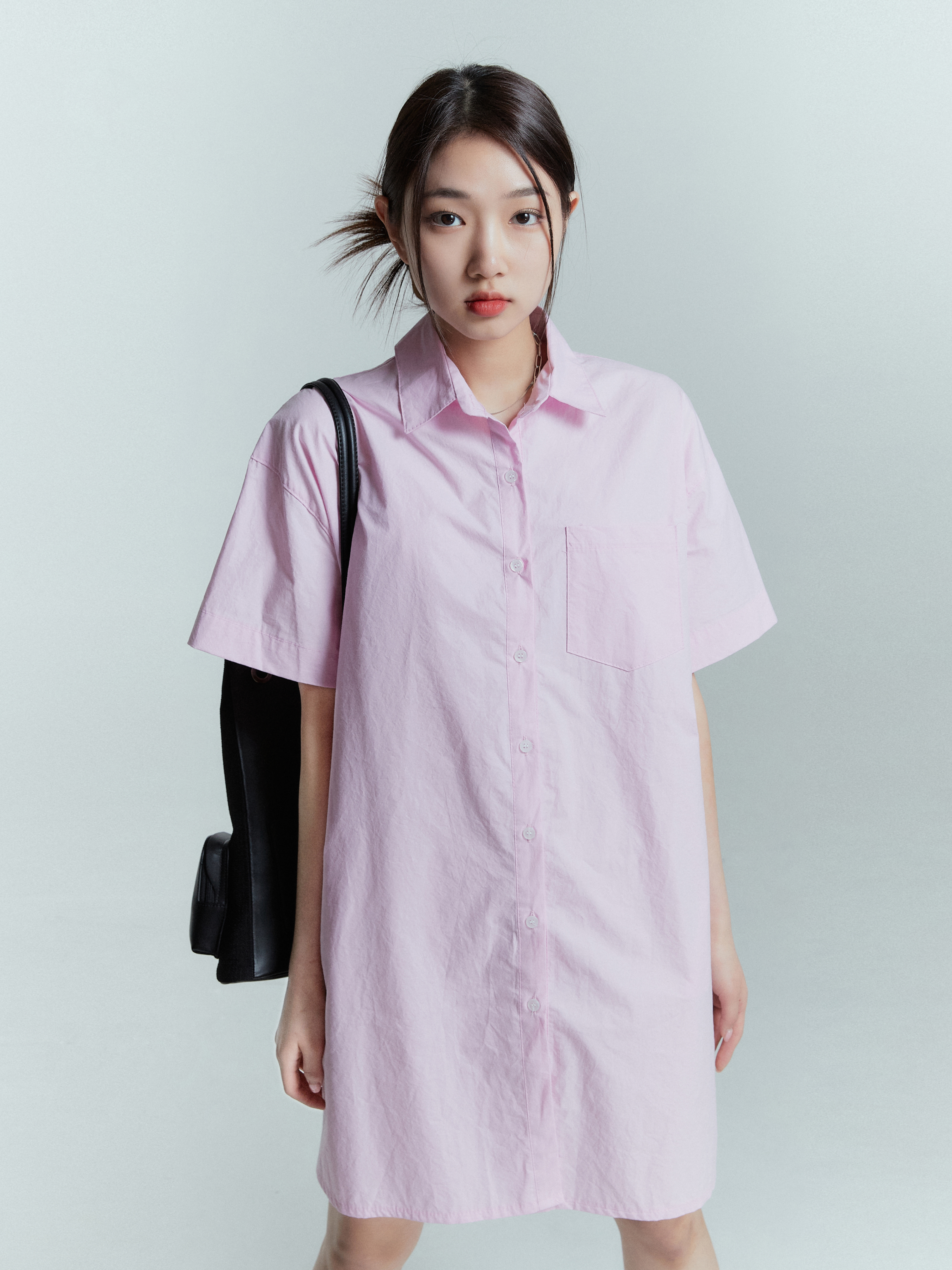 A medium shot of a model wearing the pink shirt dress zooming in on the design details of the dress.