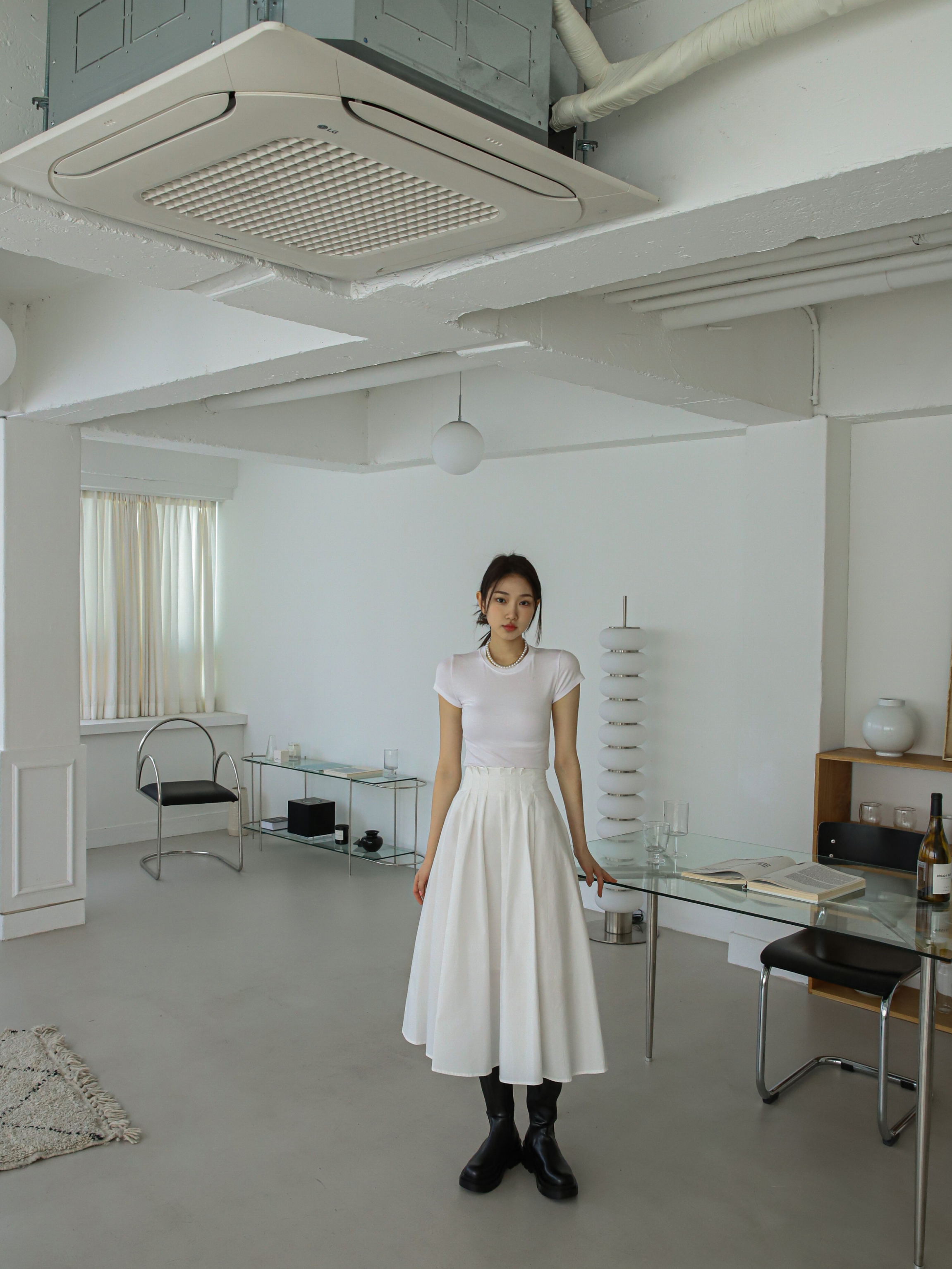 In a captivating long shot, the model effortlessly pairs the ivory short-sleeve T-shirt with a pleated midi skirt, creating a stylish and harmonious ensemble.