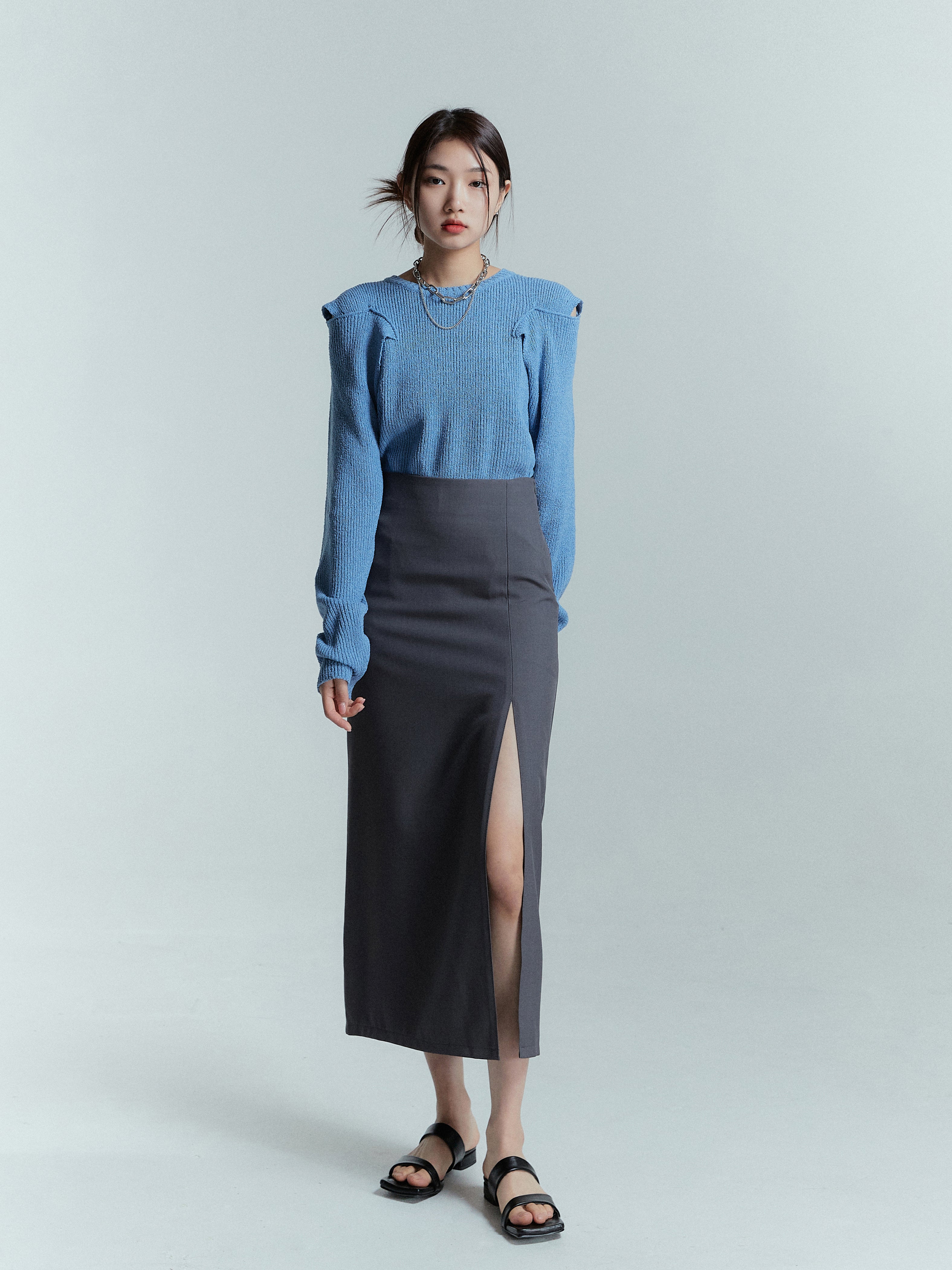 Strike a confident standing pose as the model effortlessly styles the blue shoulder cut sweater with a slit midi skirt, showcasing a fashion-forward and trendy look.