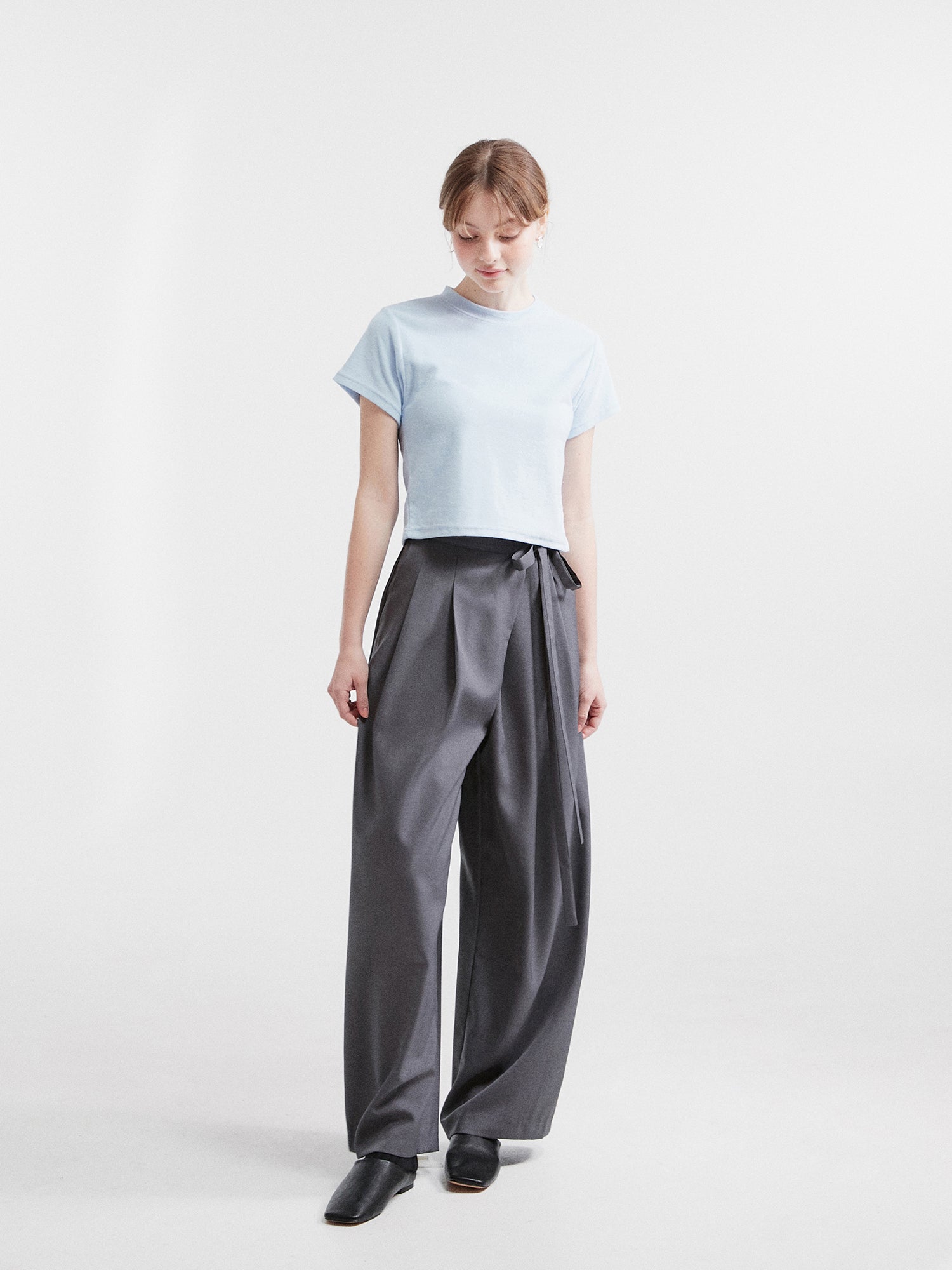 The model elegantly showcases the side-belted trousers, her gaze gracefully directed downward.