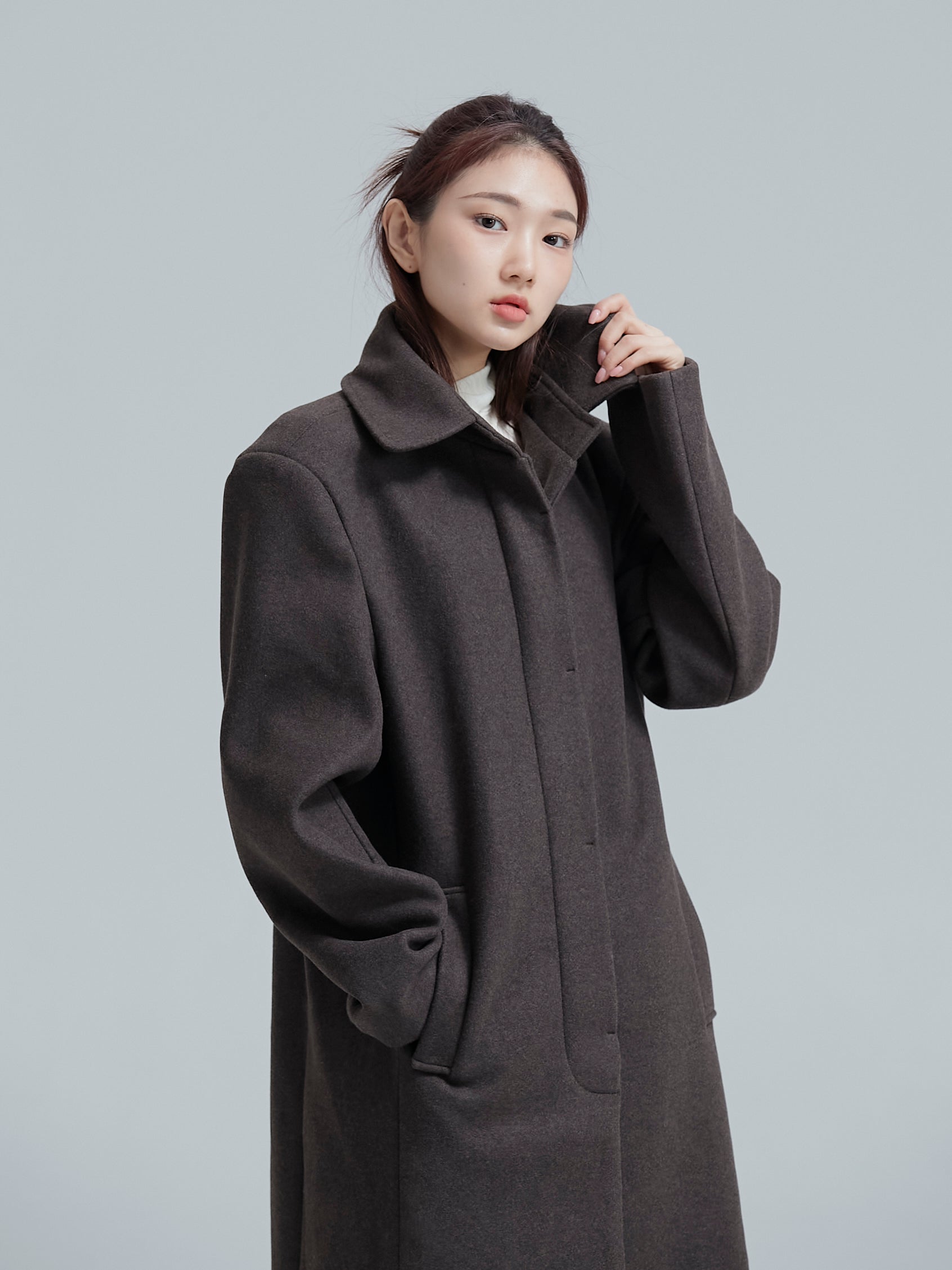 The model is elevating the collar of its single-breasted overcoat, presenting Korean aesthetic outfits with flair.