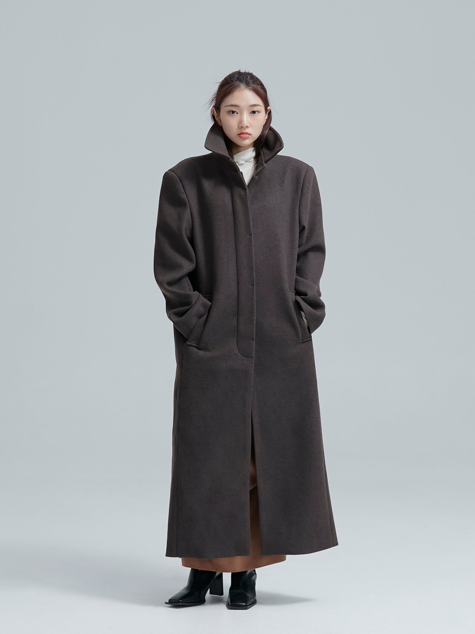 The model is standing still while wearing the single breasted overcoat with its buttons closed.